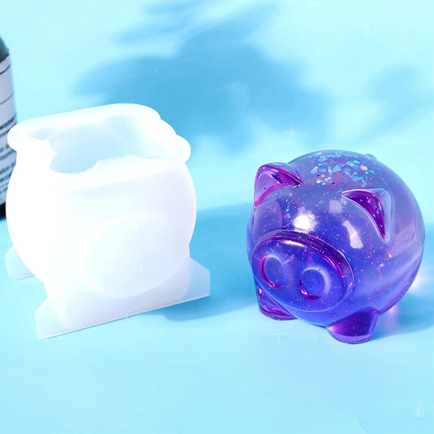 Zwei Spardosen auf einer blauen Oberfläche: eine durchscheinbare lila glitzernde Spardose und eine schlichte weiße Form oder Verpackung daneben.