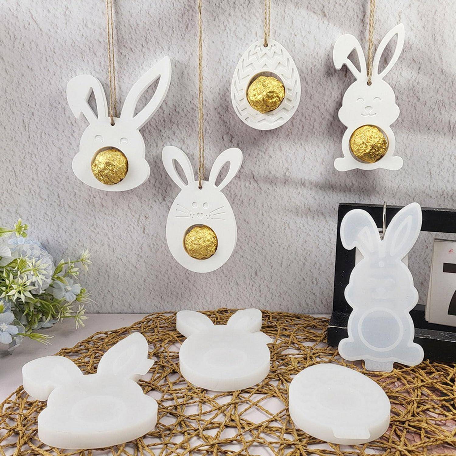 Weiße Osterdekorationen in Kaninchenform mit goldenen Eiermittelpunkten, die an einer Wand hängen, mit passenden Hasenformen oder Kerzenhaltern auf einer gewebten Matte darunter.