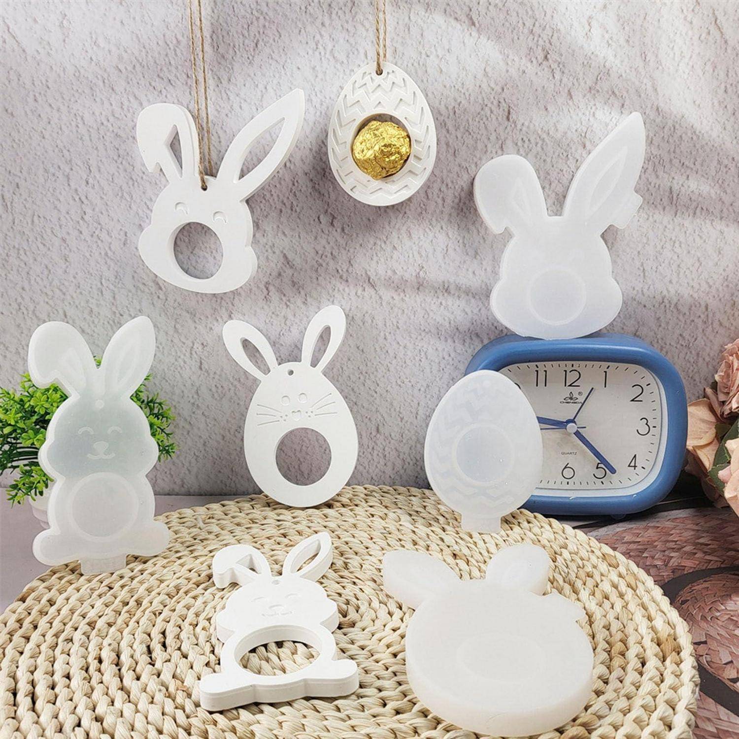 Sammlung von weißen hasenförmigen Osterdeko und Eierverzierungen auf einer geflochtenen Matte um eine blaue Uhr herum.