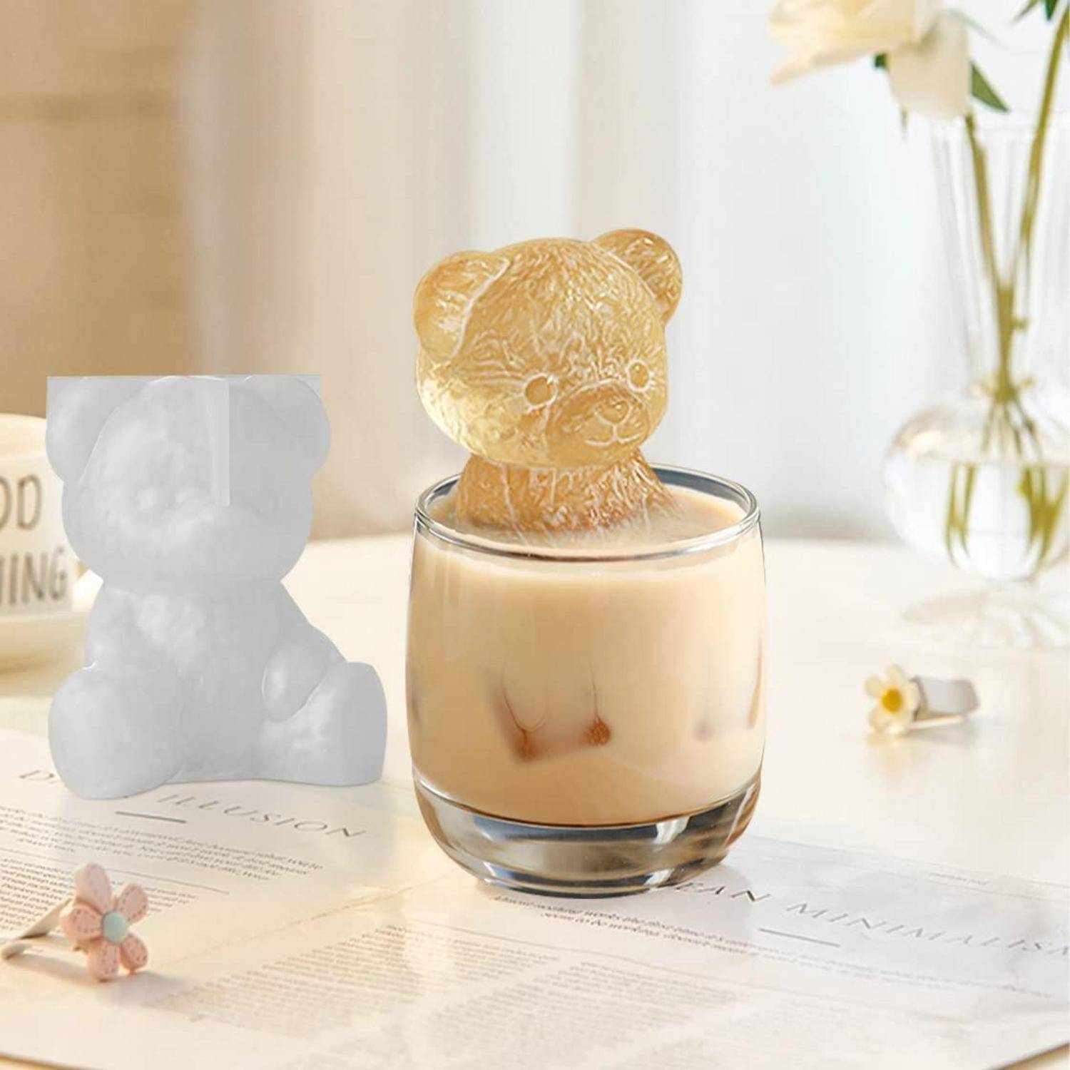 Glas Milch mit einem bärenförmigen Eiswürfel auf einer hellen Tischplatte, daneben eine weiße Bärenfigur.