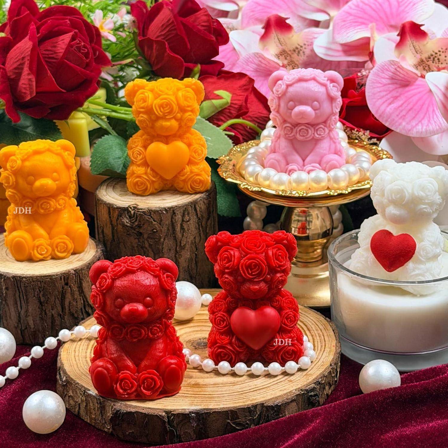 Bunte Kerzen in Teddybärform in Rot, Orange, Rosa und Weiß sind auf Holzscheiben und einem goldenen Ständer zwischen Rosen und Perlenperlen arrangiert.