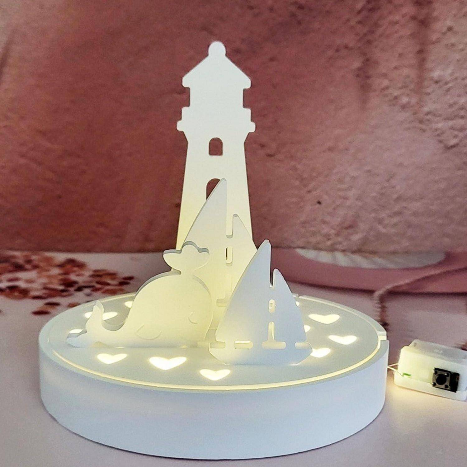 Ein beleuchteter dekorativer Pop-up-Leuchtturm aus Papier auf einer runden Basis mit Meerestier-Silhouetten und sanft leuchtenden ausgeschnittenen Herzen.