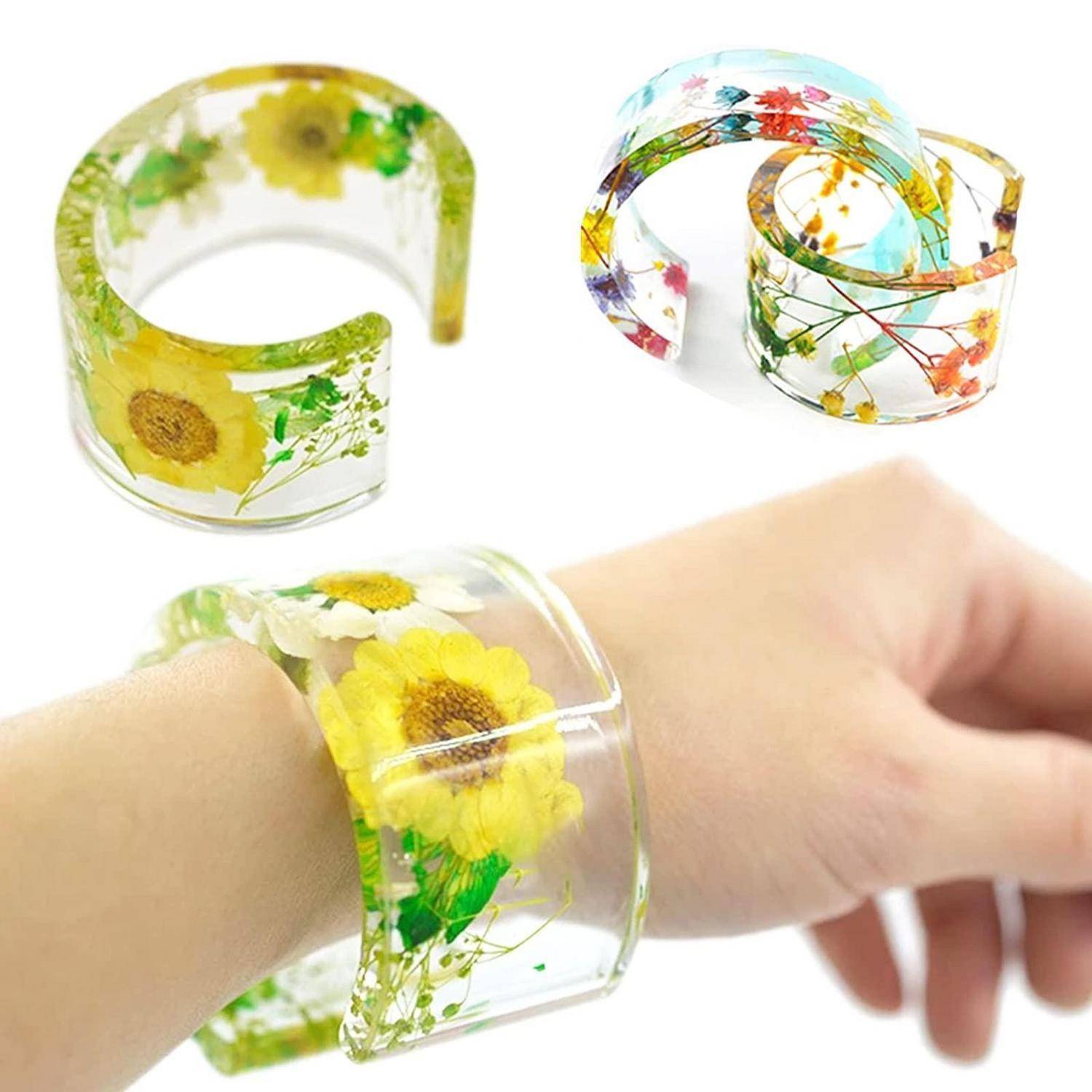 Transparente Blüten-Harz-Manschettenarmbänder, einschließlich eines an einem Handgelenk getragenen, mit gepressten Blüten im Inneren eingebettet.