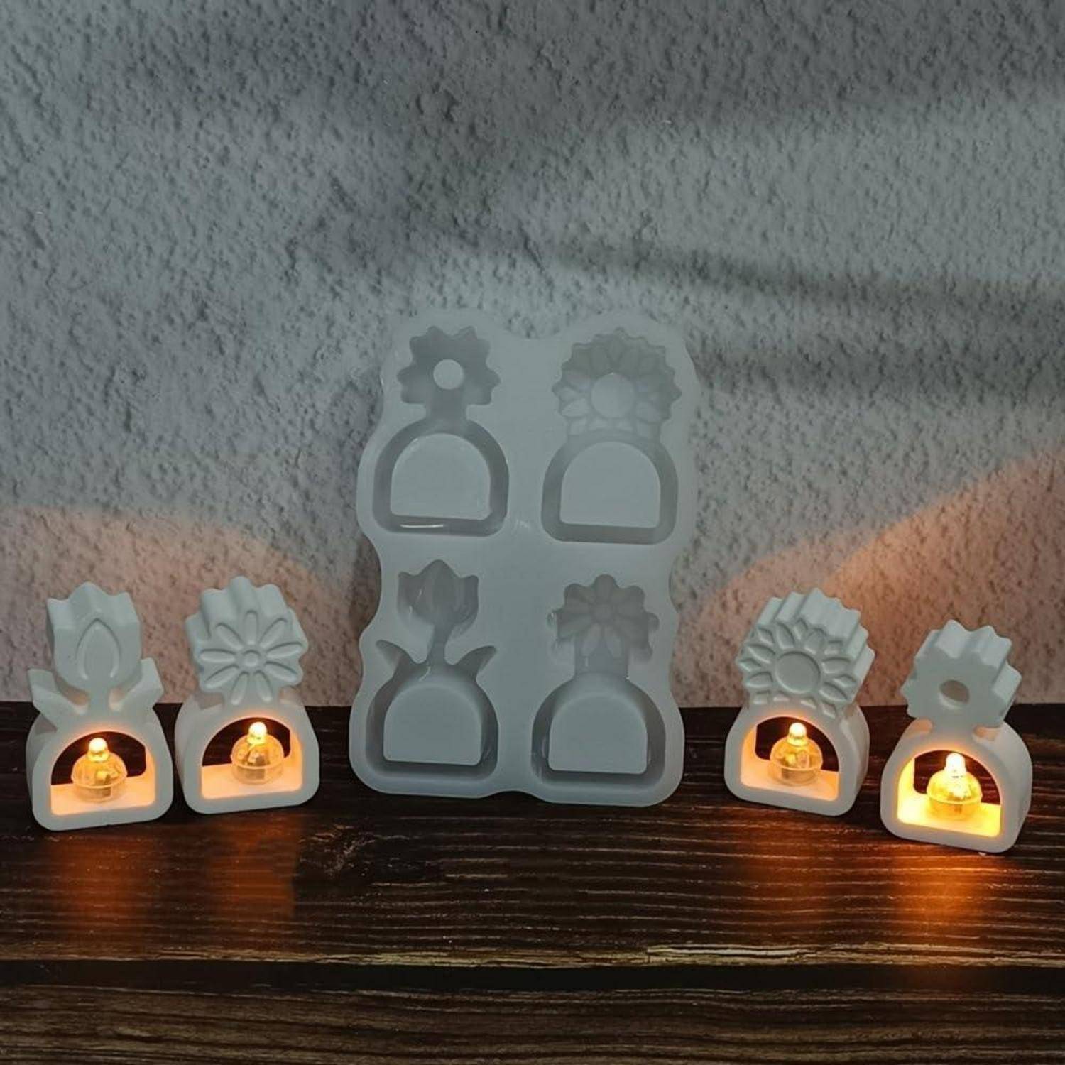 Weiße keramische blumenförmige Teelichhalter und ein Formensatz auf einer Holzoberfläche angezeigt, mit brennenden Kerzen, die in vier Haltern glühen.