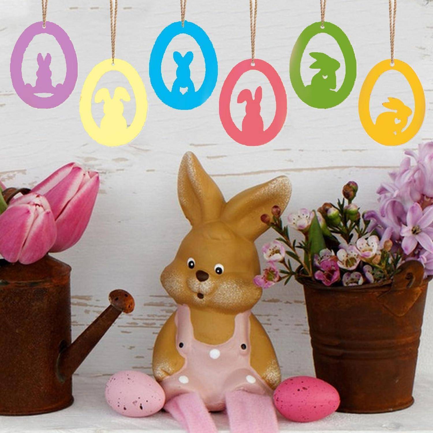 Dekorative Osterausstellung mit einer Hasenfigur, bemalten Eiern, Blumen und farbenfrohen hängenden Hasenausschnitten.