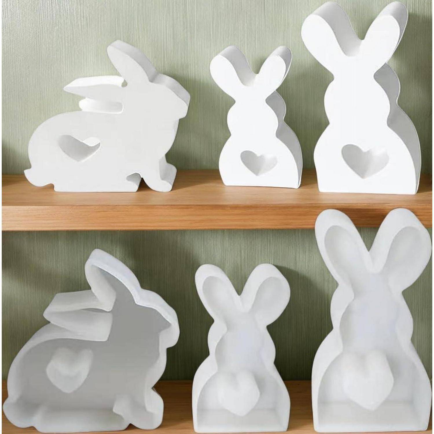 Weiße Hasen-förmige Deko-Figürchen in verschiedenen Größen, die auf Holzregalen vor einer grünen Wand angezeigt werden, jedes mit einem Herzausschnitt.