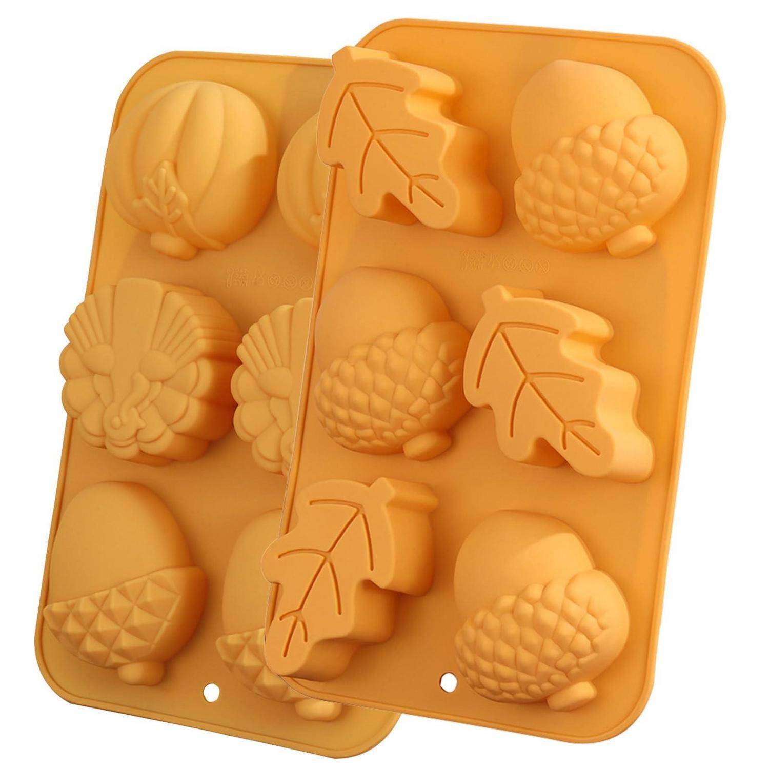 Zwei orange Silikonbackformen mit verschiedenen herbstförmigen Vertiefungen, einschließlich Blätter, Tannenzapfen und Eicheln.
