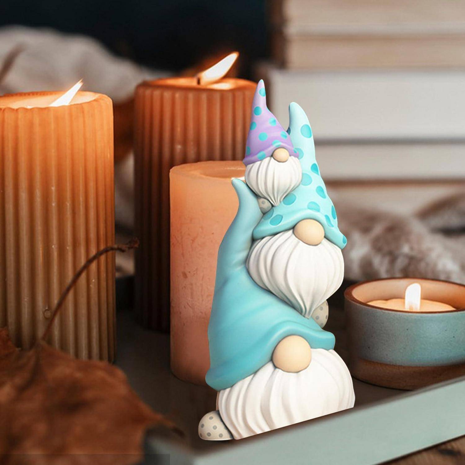 Dekorative Gnom-Figur mit blauen und violetten Hüten auf einem Tablett zwischen brennenden Kerzen und Herbstdekoration.