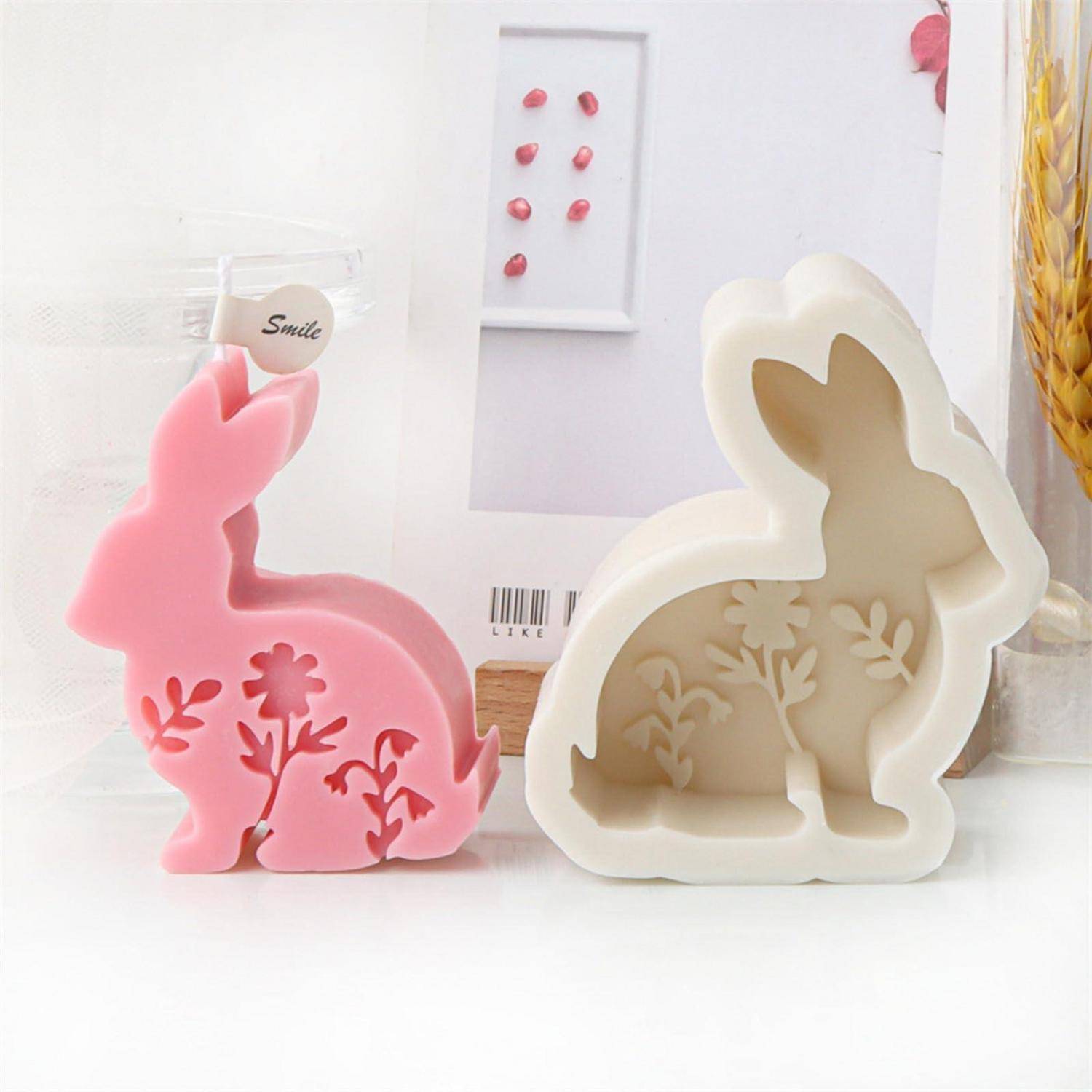Zwei dekorative kaninchenförmige Behälter oder Kerzenformen, eine rosa und eine creme, mit floralen Ausschnittsmustern auf einer weißen Oberfläche.