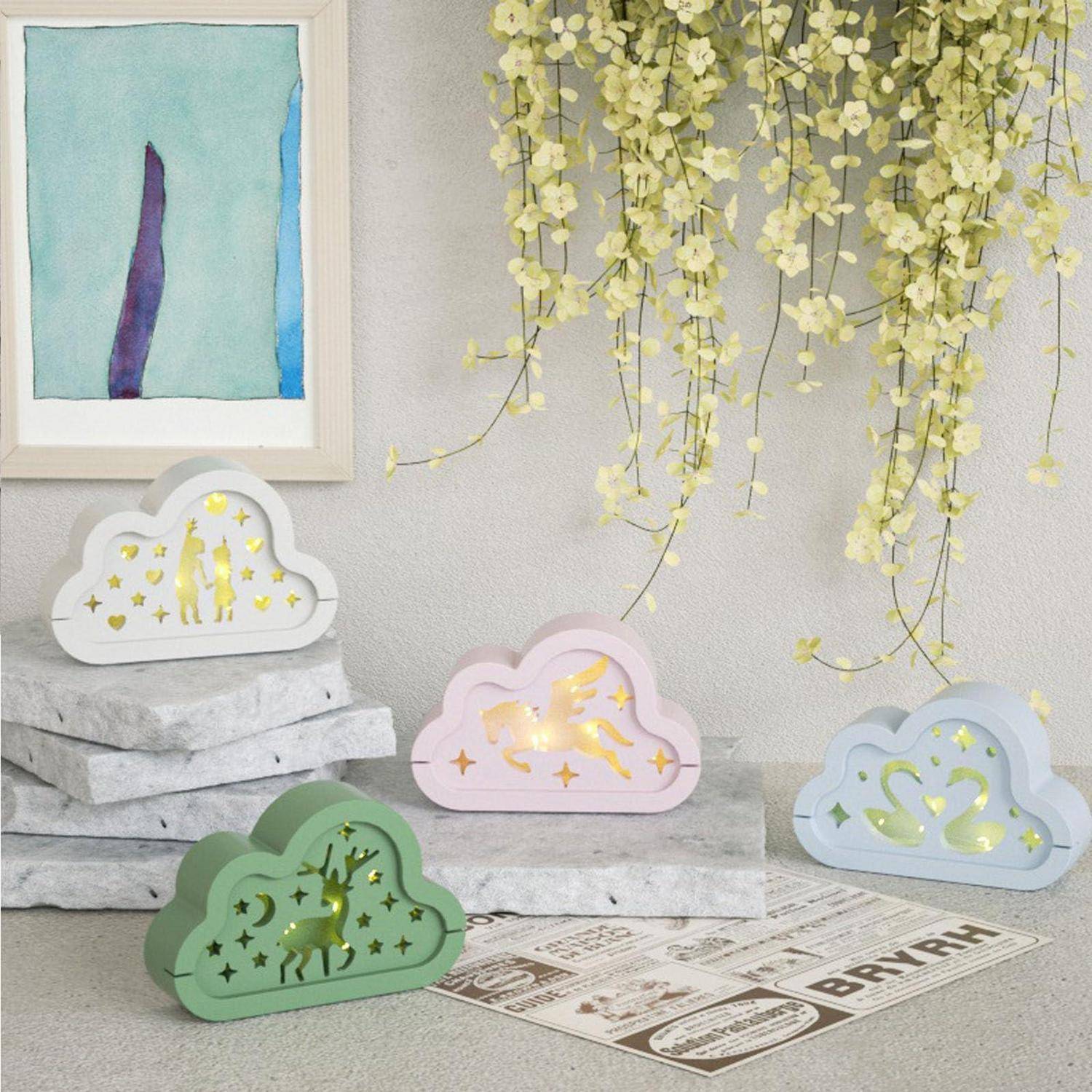 Pastellfarbene wolkenförmige Dekorationsleuchten mit ausgestanzten Sternen, Einhörnern und Herzen sitzen auf Steinblöcken unter hängenden Blumen.