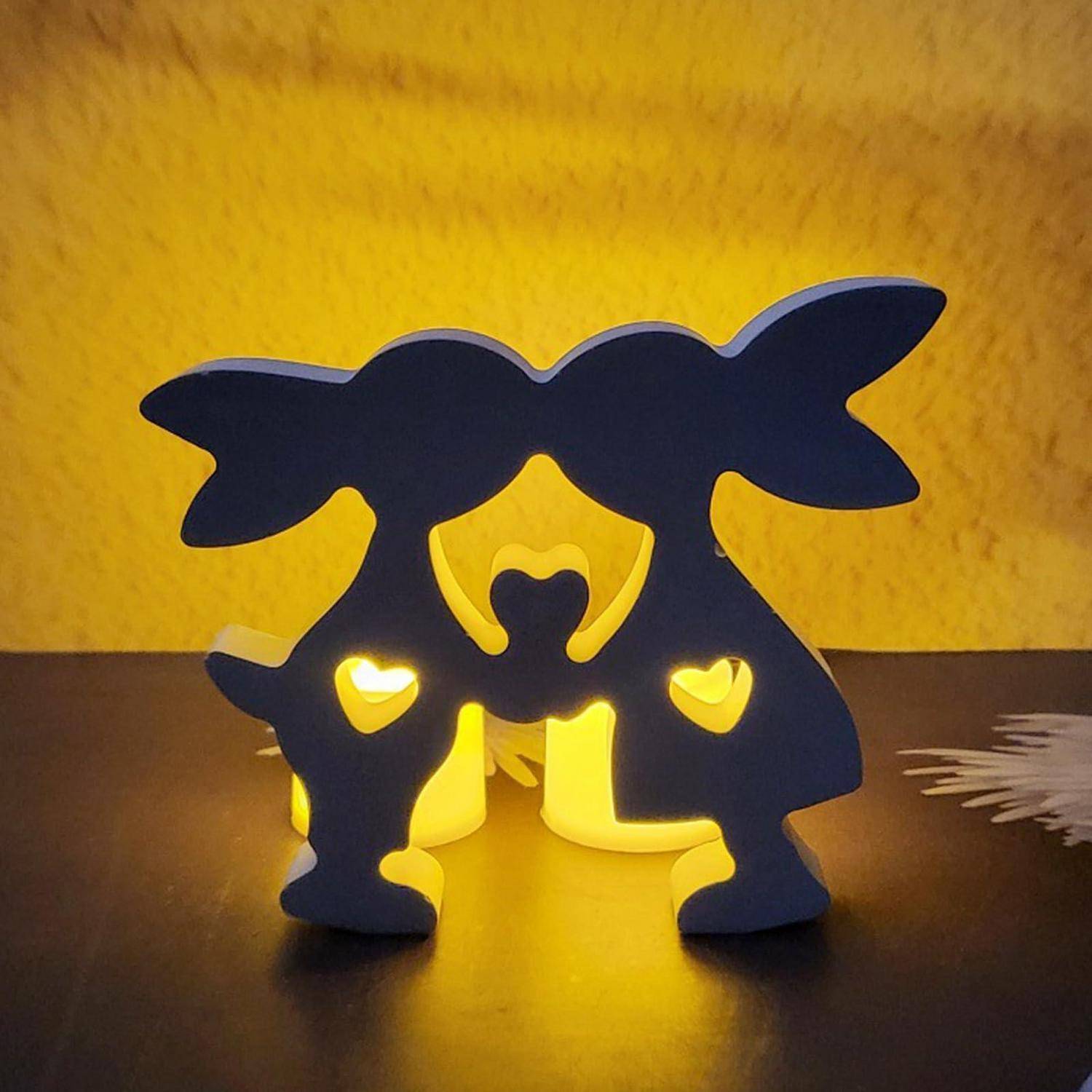Zwei dunkle dekorative Hasenschatten mit leuchtenden herzförmigen Ausschnitten stehen vor einem gelben Licht gegen eine strukturierte gelbe Wand.