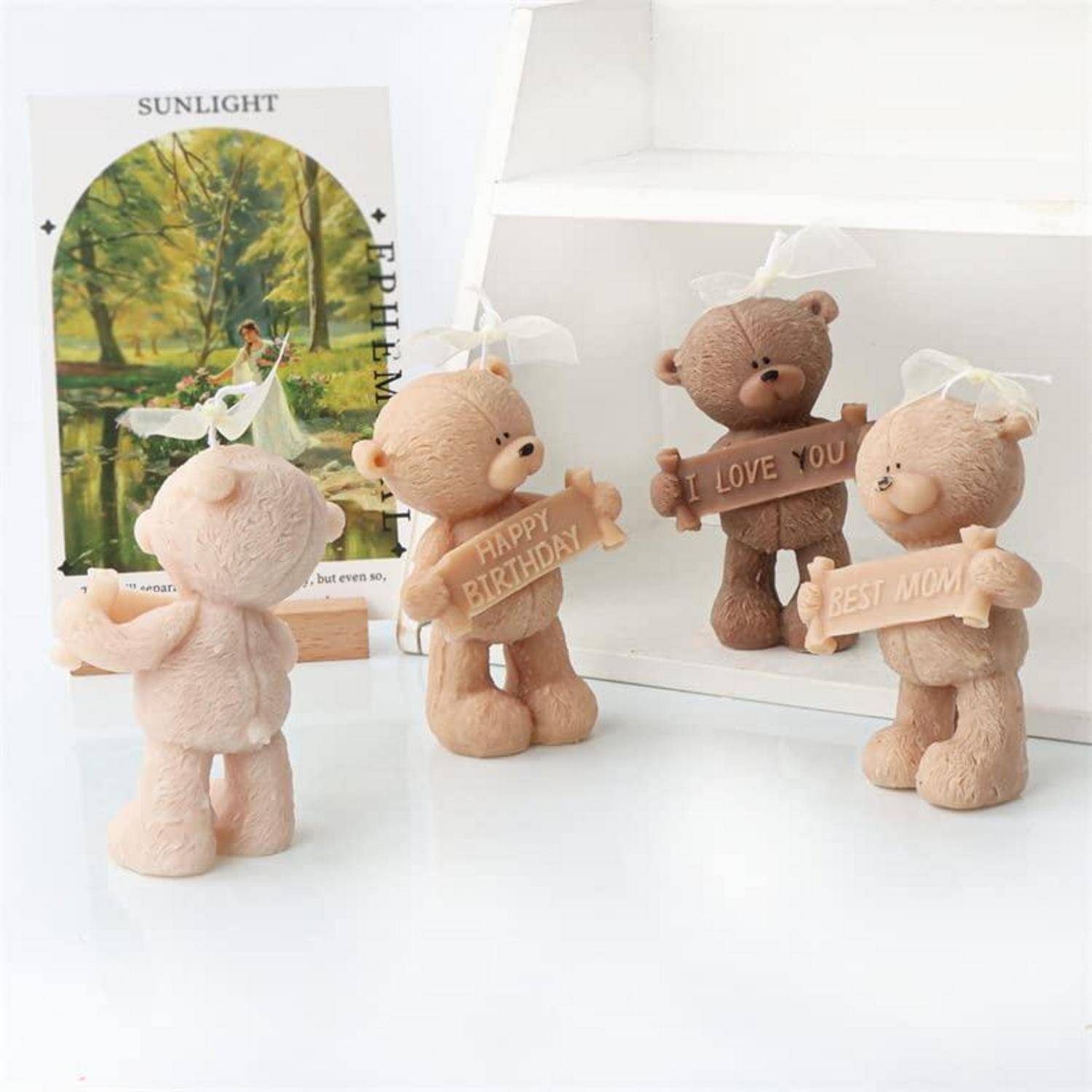 Vier Teddybär-Figuren, die Schilder halten, auf denen "ALLES GUTE ZUM GEBURTSTAG"", ""ICH LIEBE DICH"" und ""BESTE MAMA"" stehen, auf einer weißen Oberfläche.