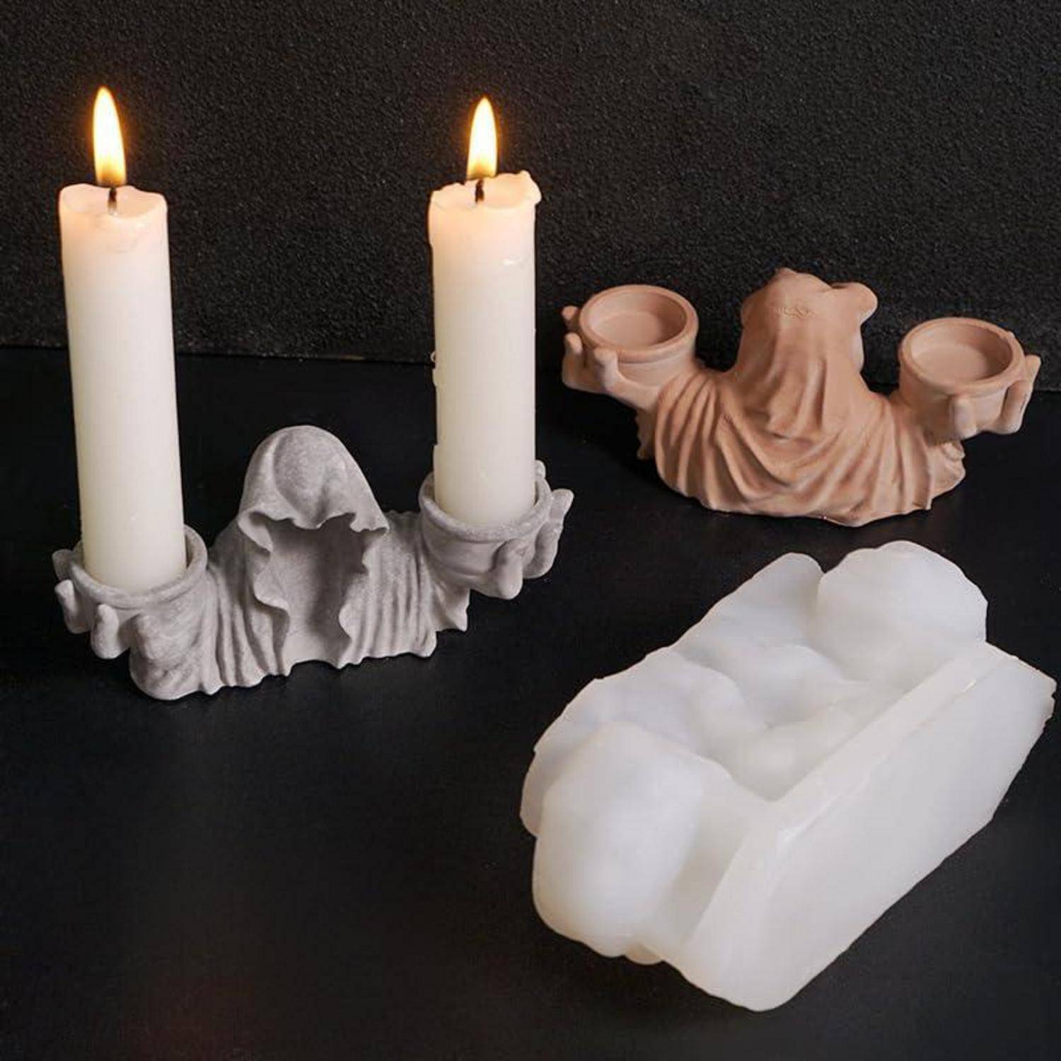 Drei Kerzenständer mit Hauben mit zwei brennenden weißen Kerzen und einem unbeleuchteten cremefarbenen Ständer auf einer dunklen Oberfläche.