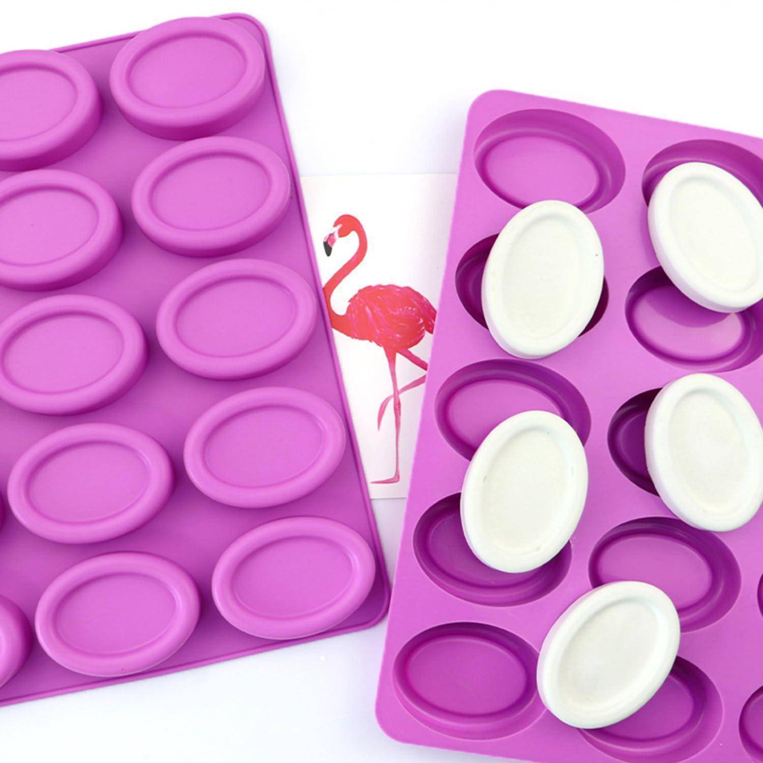 Zwei violette Silikonform-Tabletts mit ovalen Mulden, eines gefüllt mit weißen ovalen Teilen, auf weißem Hintergrund mit einer teilweise sichtbaren rosa Flamingo-Illustration zwischen ihnen.