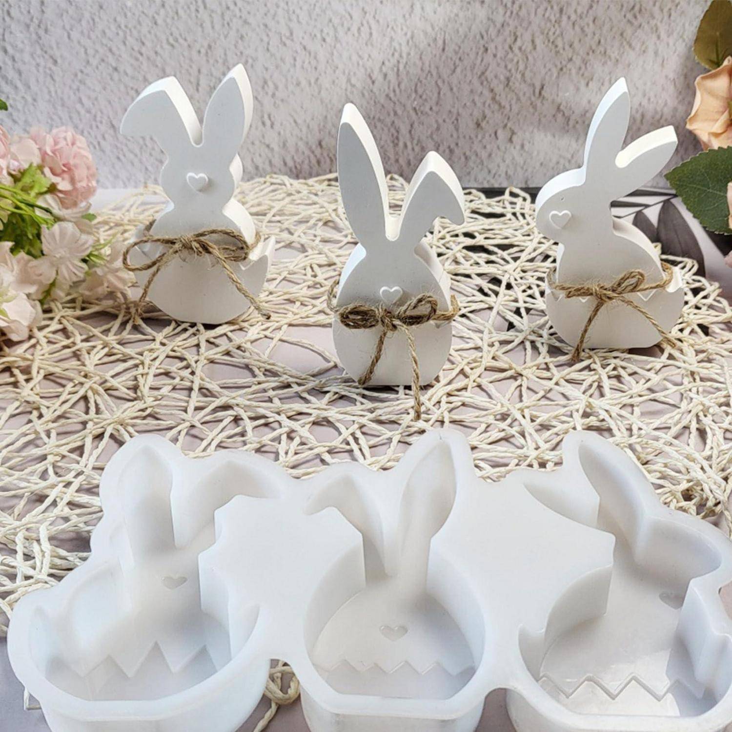 Weiße hasenförmige Osterdekoration und kleine weiße Hasengeschenkboxen mit Schnur gebunden, arrangiert auf einer geflochtenen Matte.