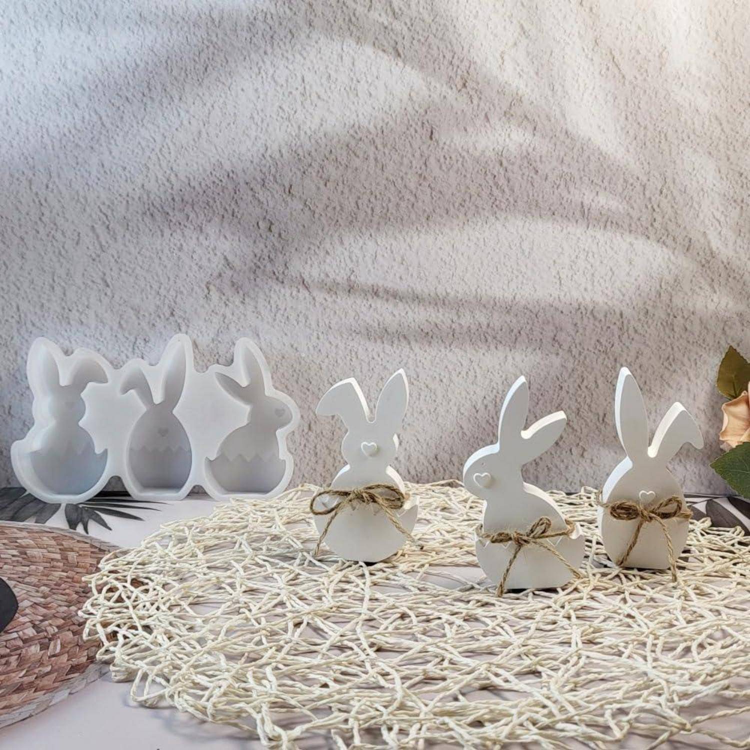 Dekorative Osterhasen-Figuren und Ausschnitte, mit Schnur gebunden, auf einer gewebten Matte angeordnet mit Blumen im Hintergrund.