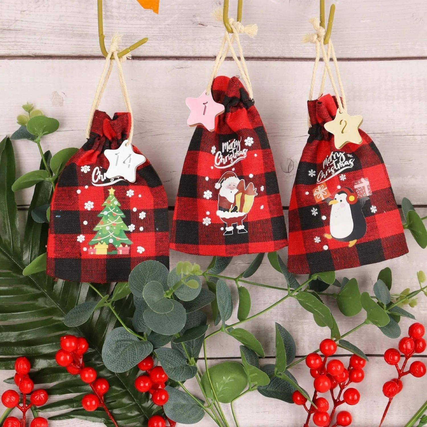 Drei karierte Weihnachtsgeschenktüten hängen an einer Holzwand, verziert mit Baum-, Weihnachtsmann- und Pinguinmotiven sowie Sternanhängern, umgeben von grünem Laub und roten Beeren.