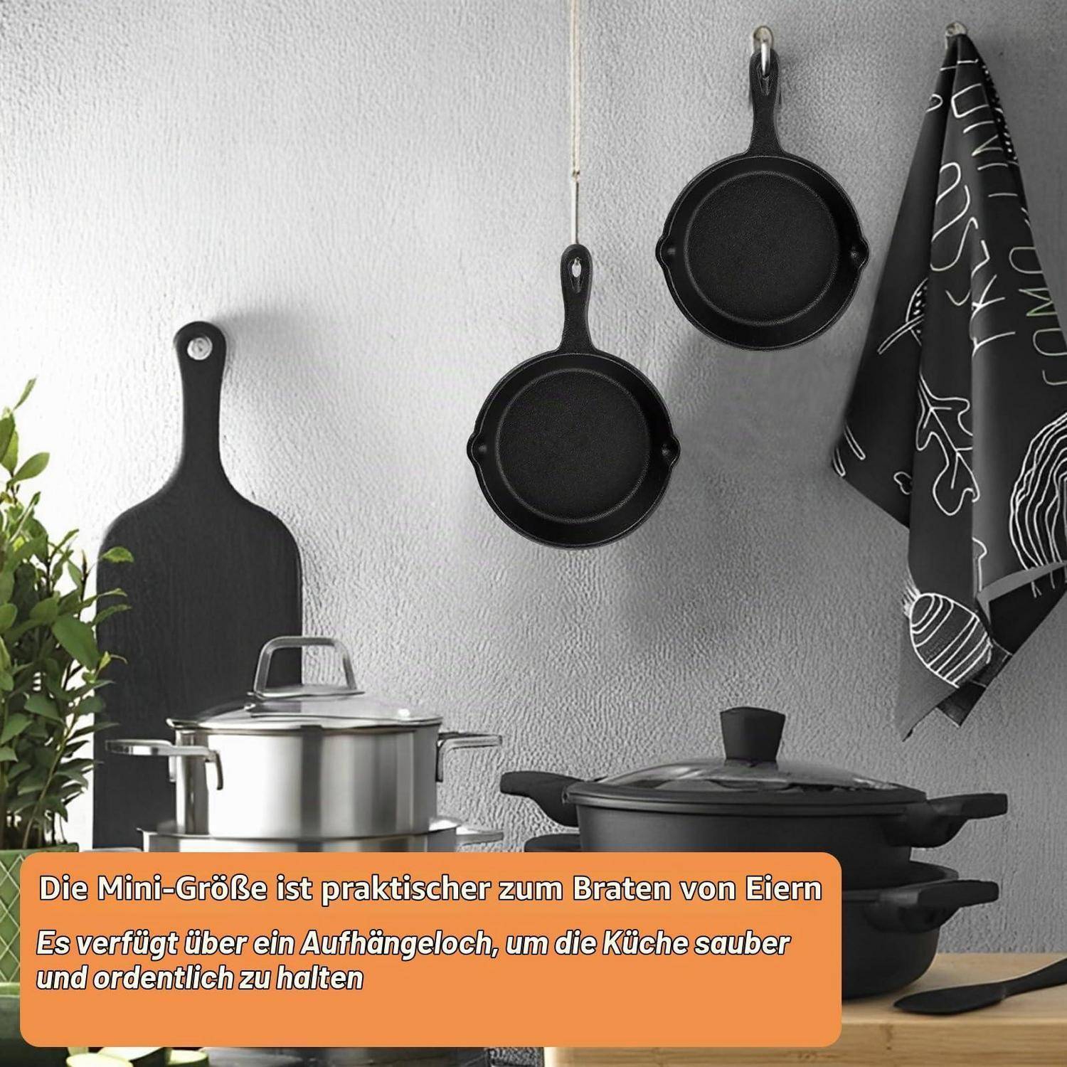 Küchenausstattung mit kleinen schwarzen Pfannen und Kochgeschirr, die an einer Wand hängen, mit einer Bildunterschrift auf Deutsch über die Mini-Größe, die praktisch zum Spiegeleibraten ist und einfach aufzuhängen für eine ordentliche Küche.