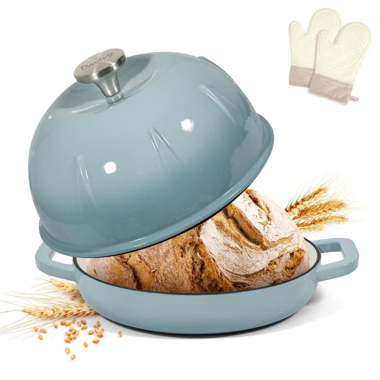 Blauer Gusseisen-Topf mit Deckel, zeigt einen runden Laib Brot beim Backen, mit Ofenhandschuhen in der Ecke auf weißem Hintergrund.