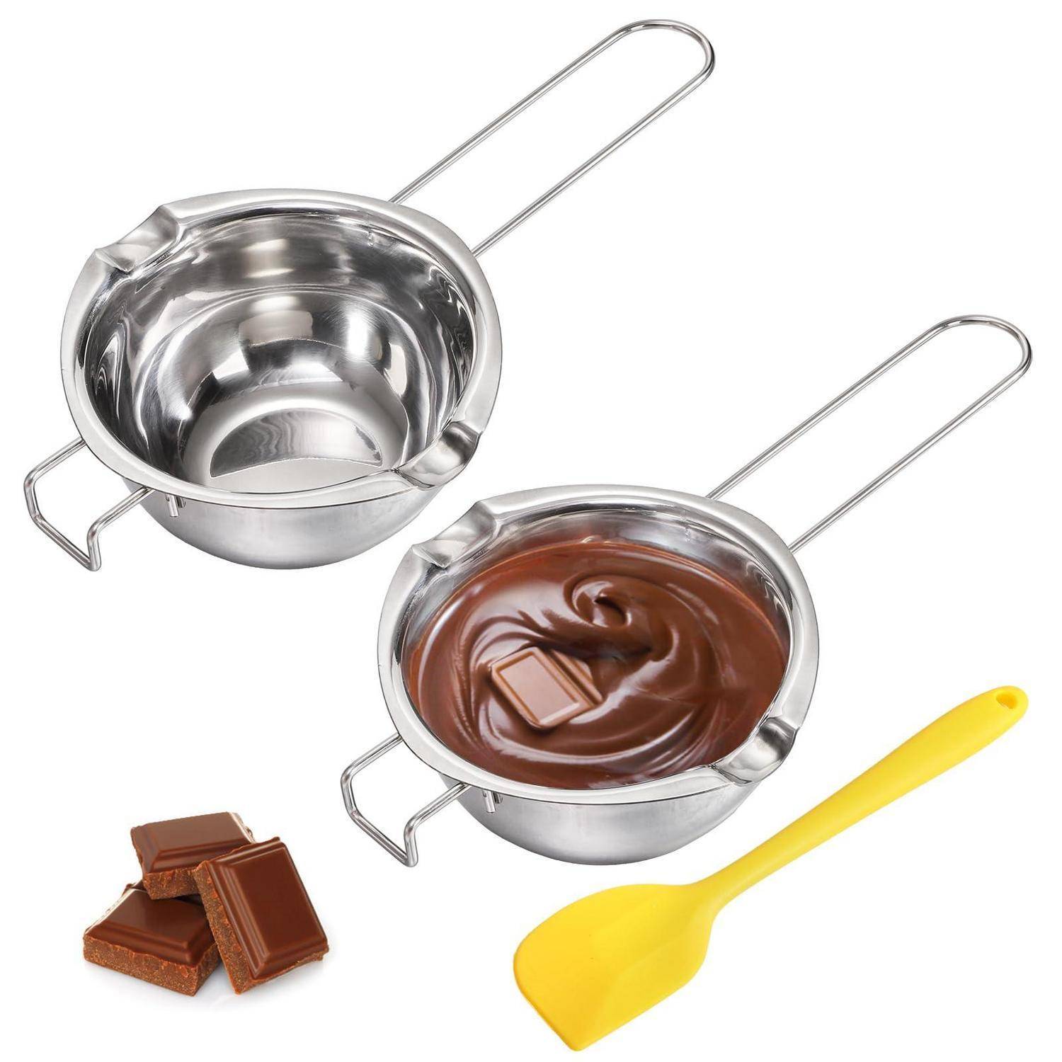 Zwei Edelstahl-Schmelztöpfe mit langen Griffen, einer leer und einer mit geschmolzener Schokolade gefüllt, plus Schokoladenstücke und ein gelber Spatel auf weißem Hintergrund.