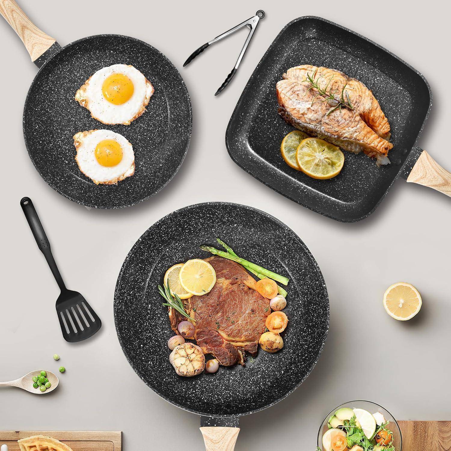 Draufsicht auf drei schwarze gesprenkelte Pfannen mit gekochtem Essen: zwei Spiegeleier, ein Lachsfilet mit Zitrone und ein Steak mit Gemüse.
