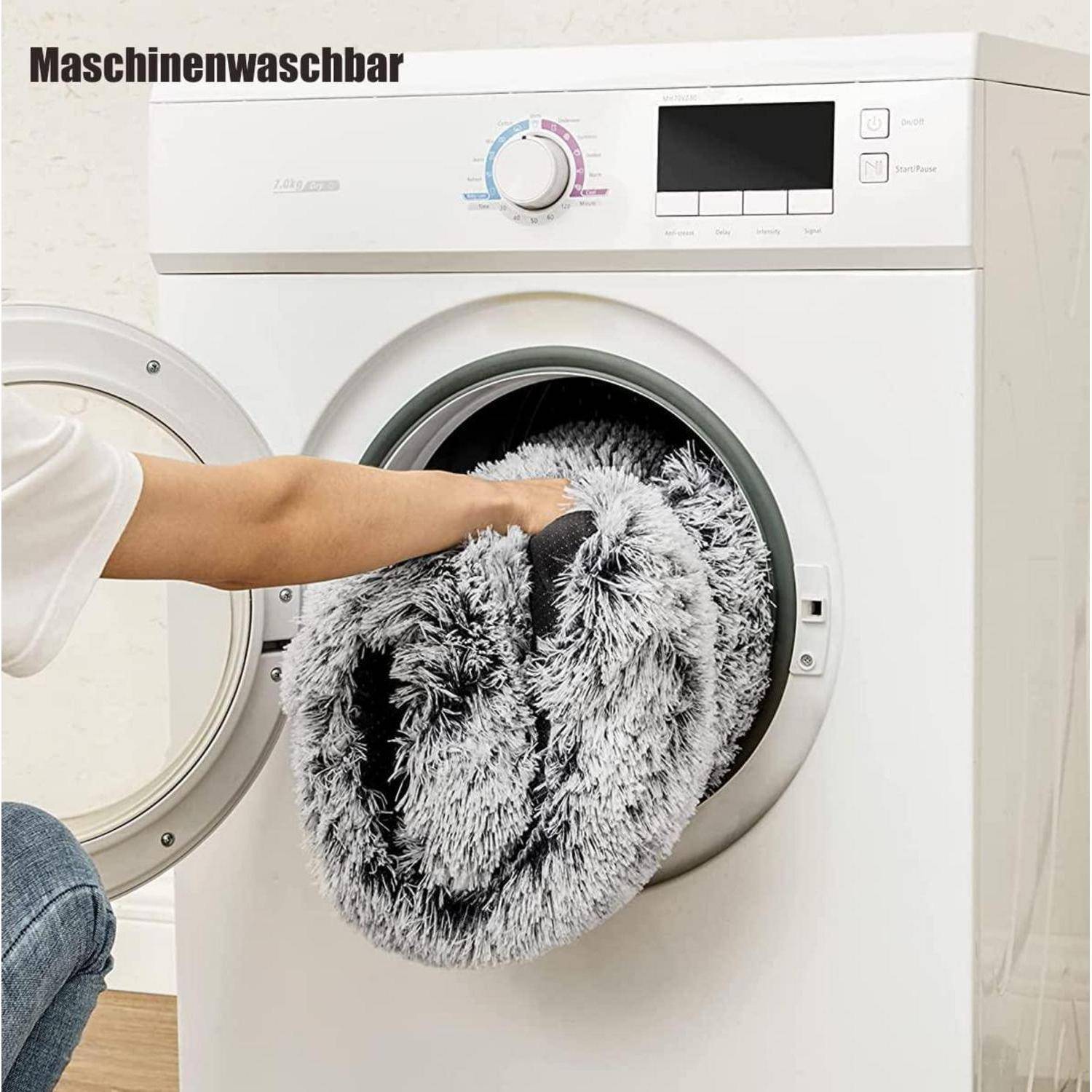 Person, die eine graue Decke in eine Frontlader-Waschmaschine laden, mit dem Etikett "Maschinenwaschbar"" oben.