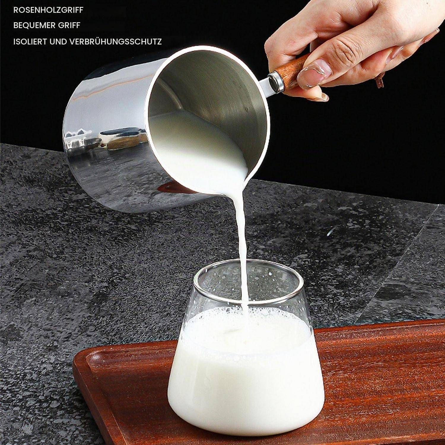 Eine Hand gießt Milch aus einem Edelstahlkrug in ein Glas auf einem Holztablett; deutscher Text hebt einen Rosenholzgriff und einen isolierten, brandschutzgerechten Griff hervor.