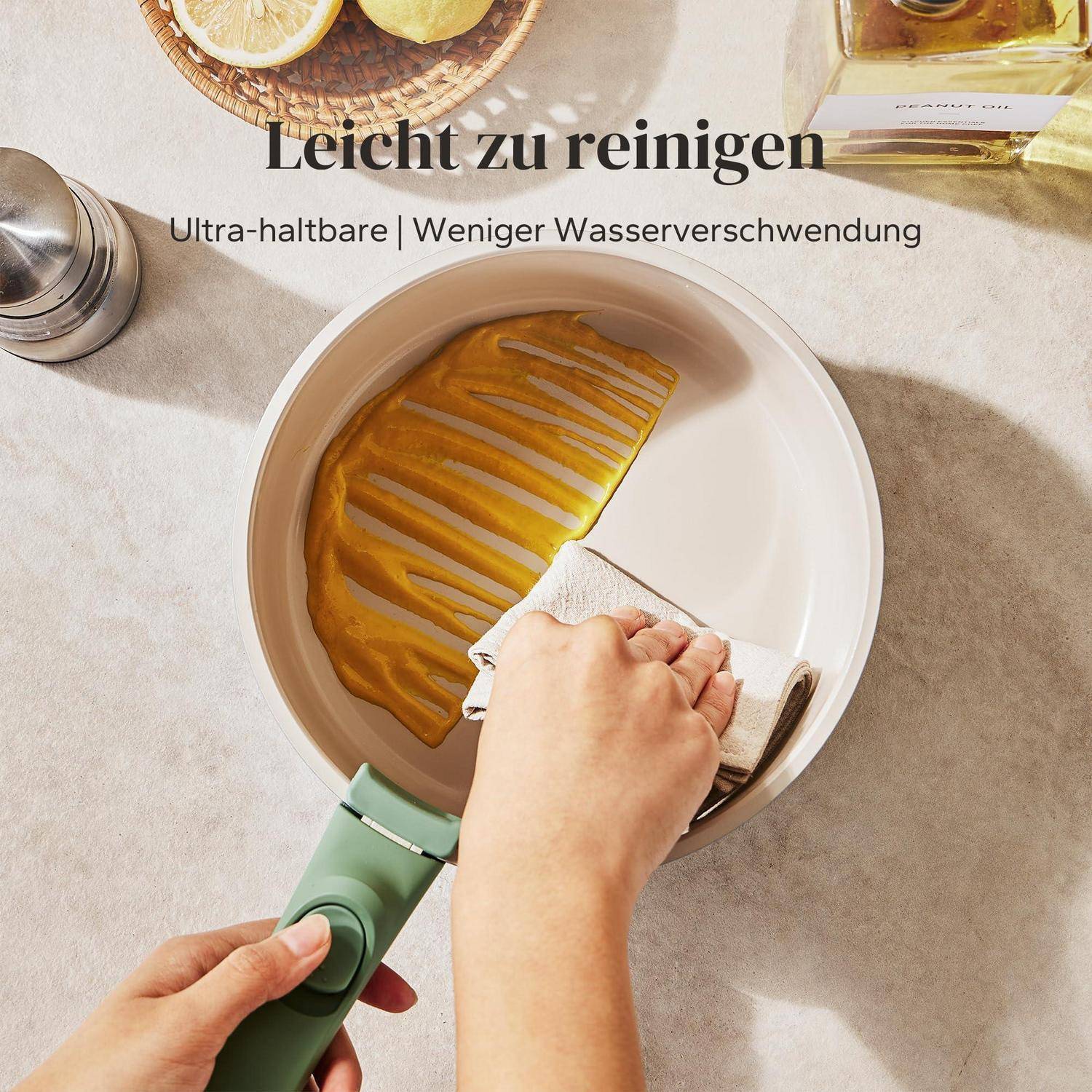Person wischt eine Antihaftpfanne mit einem Tuch ab; deutscher Text besagt „Leicht zu reinigen" und „Ultra-haltbar | Weniger Wasserverschwendung"".