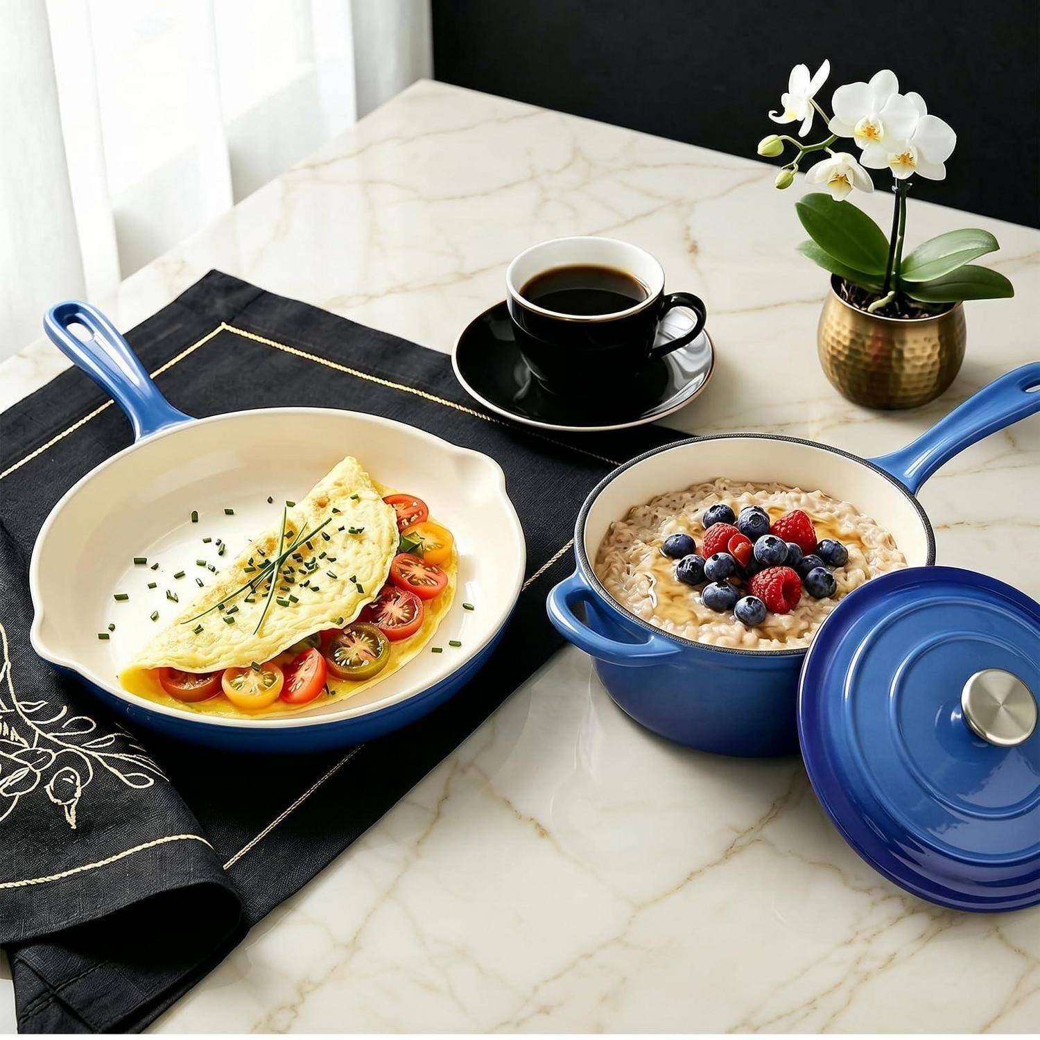 Frühstück auf einem Marmortisch: ein Omelett in einer blauen Pfanne mit Tomaten, ein mit Blaubeeren gekrönter Haferbrei-Topf und eine Tasse Kaffee neben einer kleinen Orchidee.