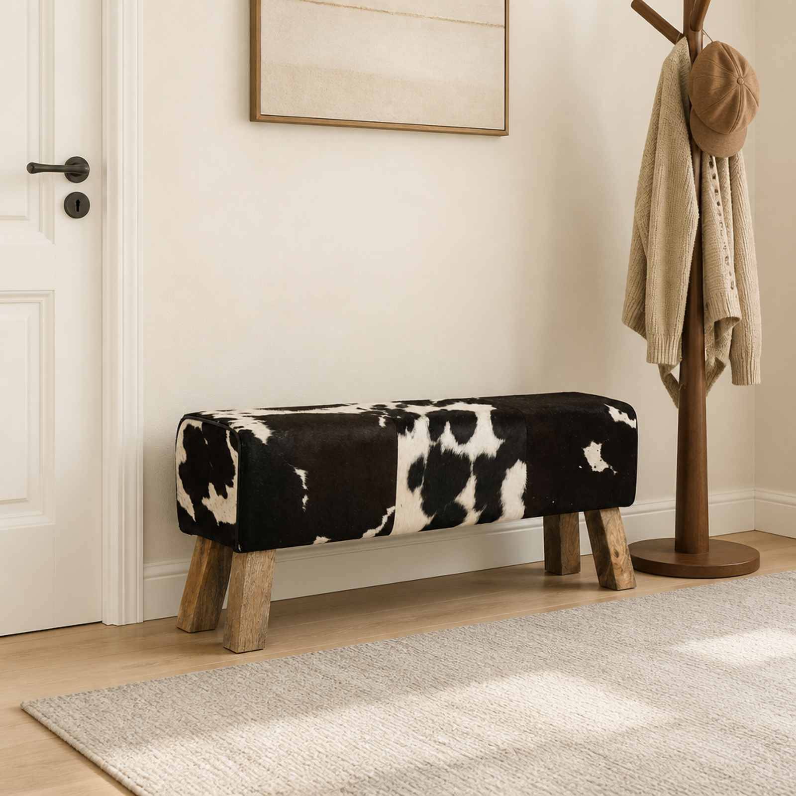 Sitzbank mit Kuhfell-Muster und Polsterung mit Holzbeinen in einem minimalistischen Eingangsbereich, neben einer Garderobe und neutraler Wandkunst.