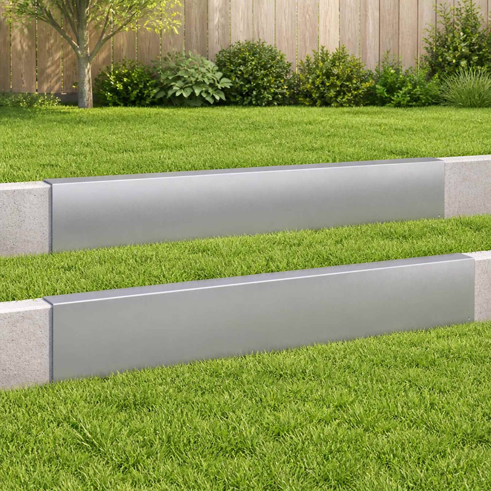 Moderner landschaftlich gestalteter Garten mit gestuften Betonmauern zur Böschungssicherung, grünem Rasen und Sträuchern vor einem Holzzaun.