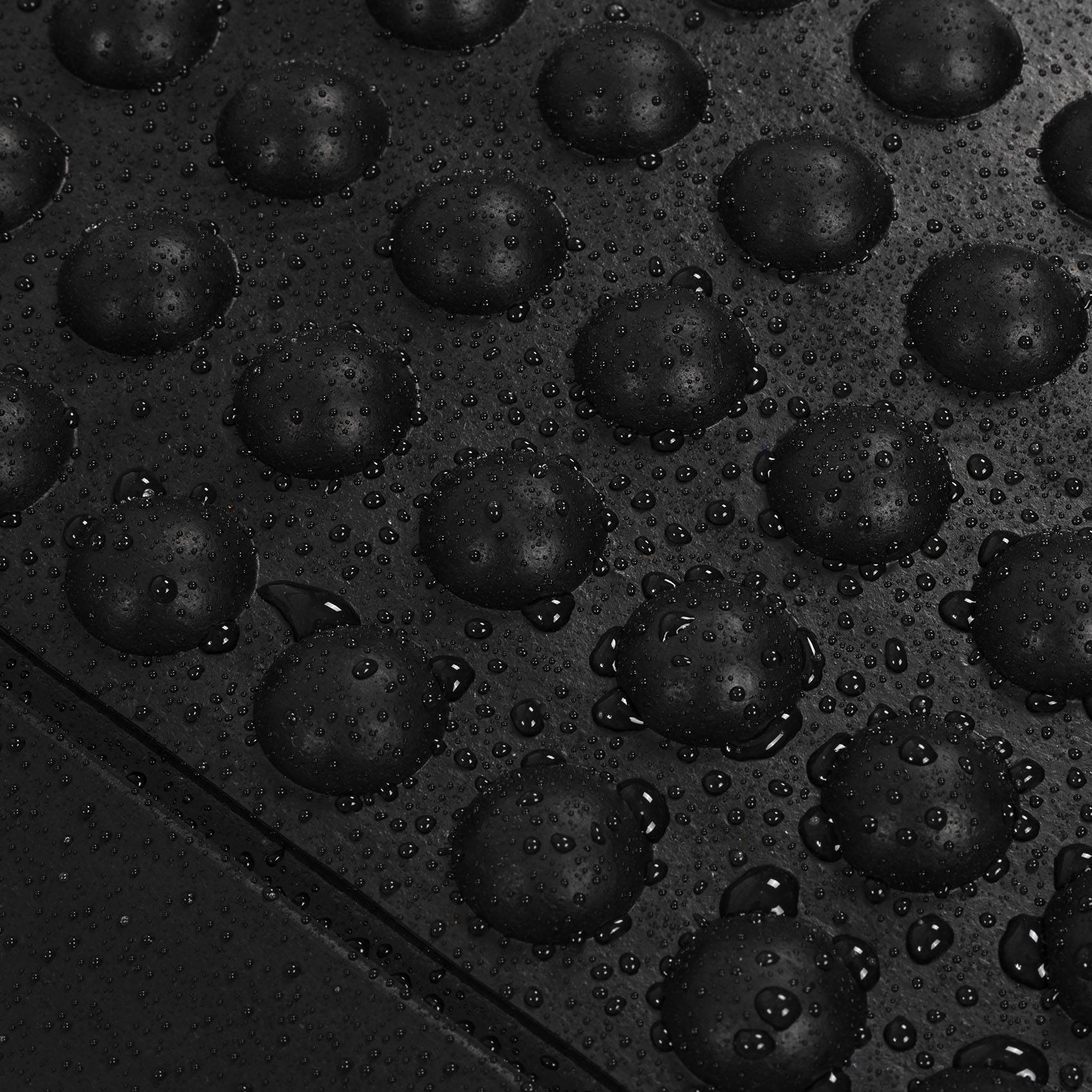Nahaufnahme einer schwarzen strukturierten Oberfläche, die mit Wassertropfen bedeckt ist, mit erhabenen kreisförmigen Erhebungen über das Material verteilt.