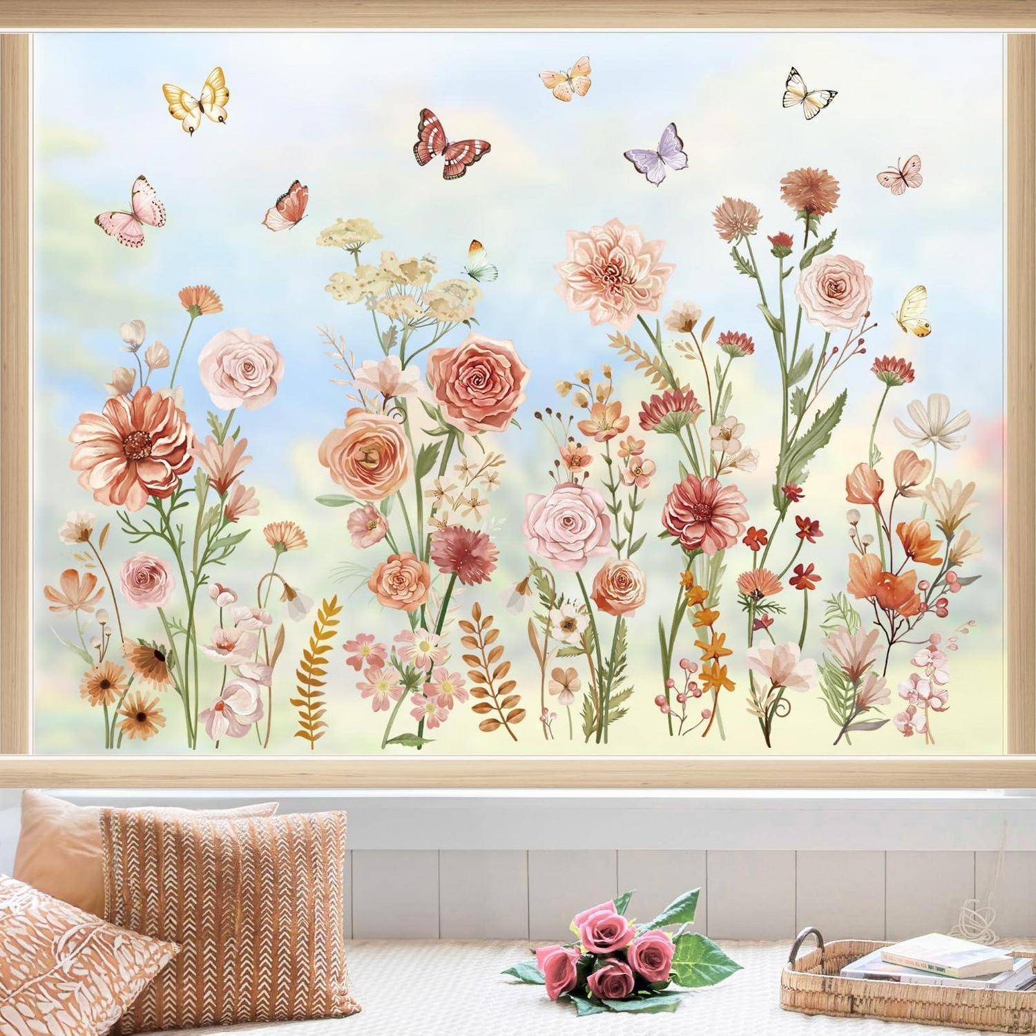 Gerahmte Wandkunst mit pastellfarbenen Wildblumen und Schmetterlingen über einem Bett mit gemusterten Kissen und einem kleinen Tablett mit Büchern und rosa Rosen.