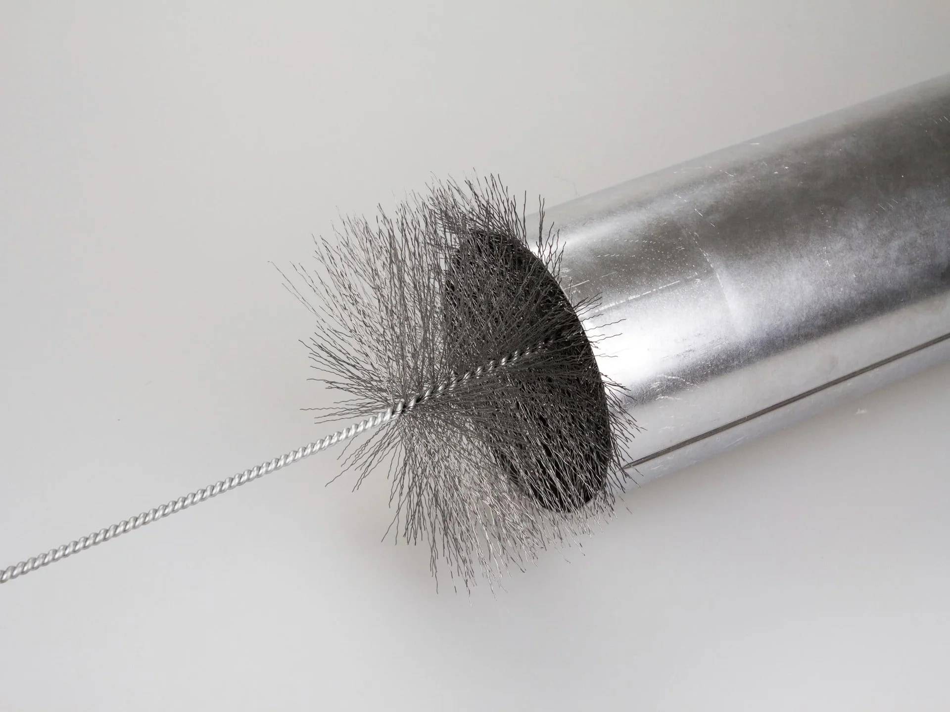 Eine Metallbürste reinigt ein silbernes zylindrisches Rohr, wobei ein dünner Draht durch seine Mitte verläuft.