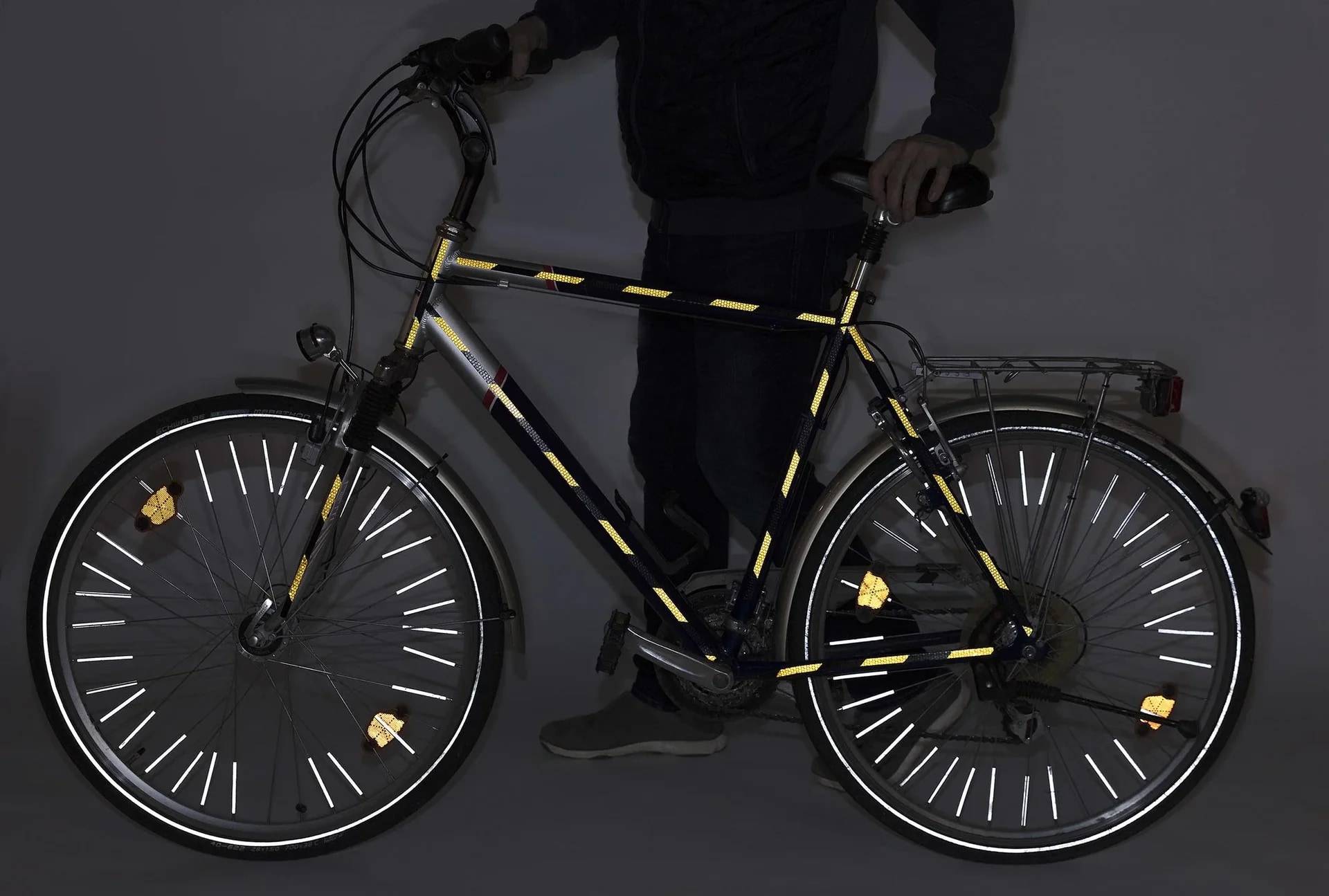 Person steht mit einem Fahrrad, das Reflektoren an dem Rahmen und an den Speichen zur Sichtbarkeit in der Nacht zeigt.