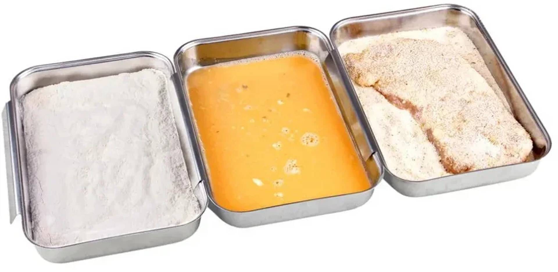Drei Edelstahl-Speisebehälter nebeneinander angeordnet, jeder mit einer anderen Zutat: weißes Pulver, orangefarbige Flüssigkeit und blassmehliges Gemisch.