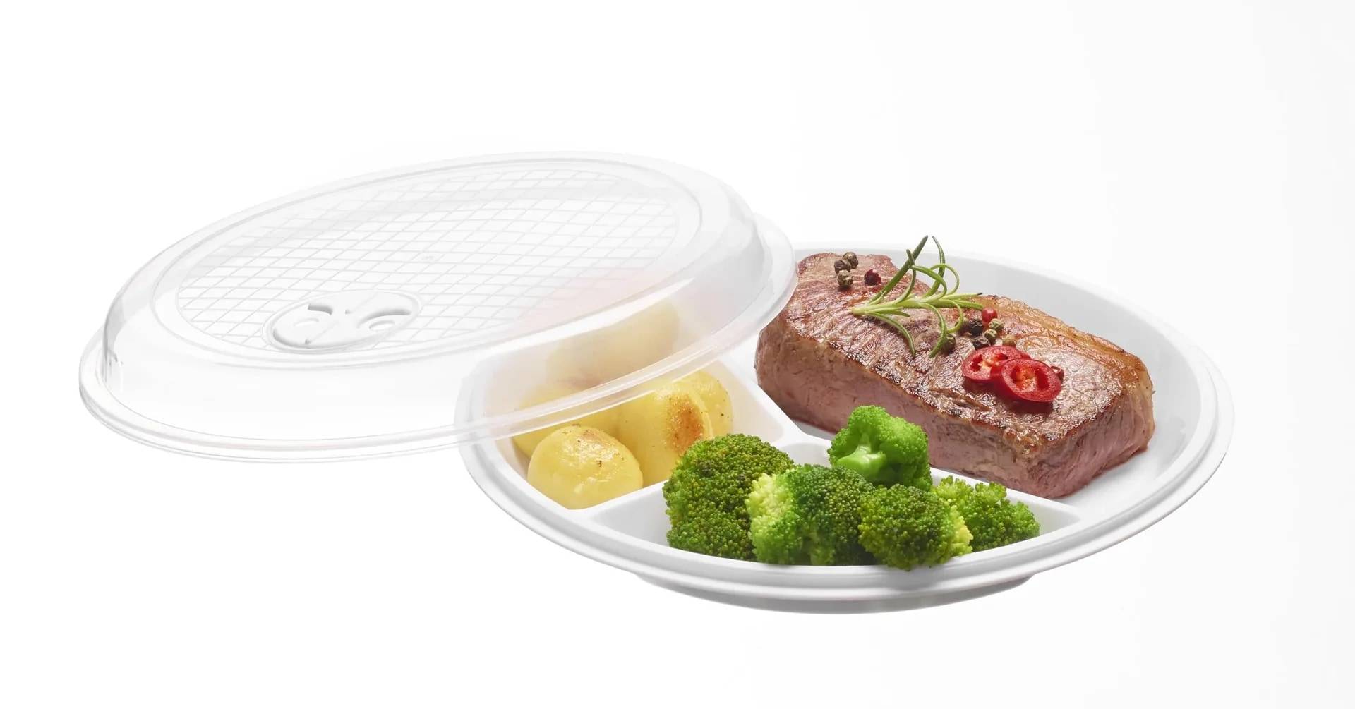 Abgedecktes Behältnis zum Mitnehmen mit Steak, Kartoffelecken und Brokkoli auf einem weißen Teller, mit einem durchsichtigen Kunststoffdeckel, der teilweise geöffnet ist.