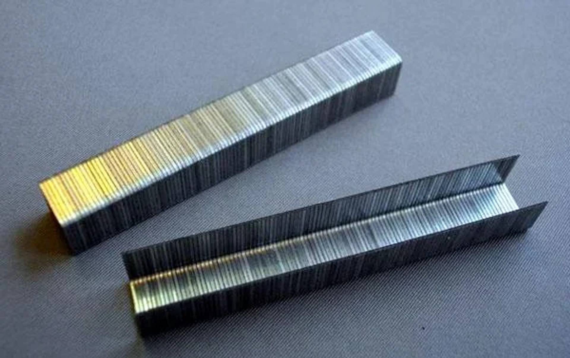 Drei Metallklammern, eine geschlossen und zwei offen gebogen, liegen auf einer grauen Oberfläche.