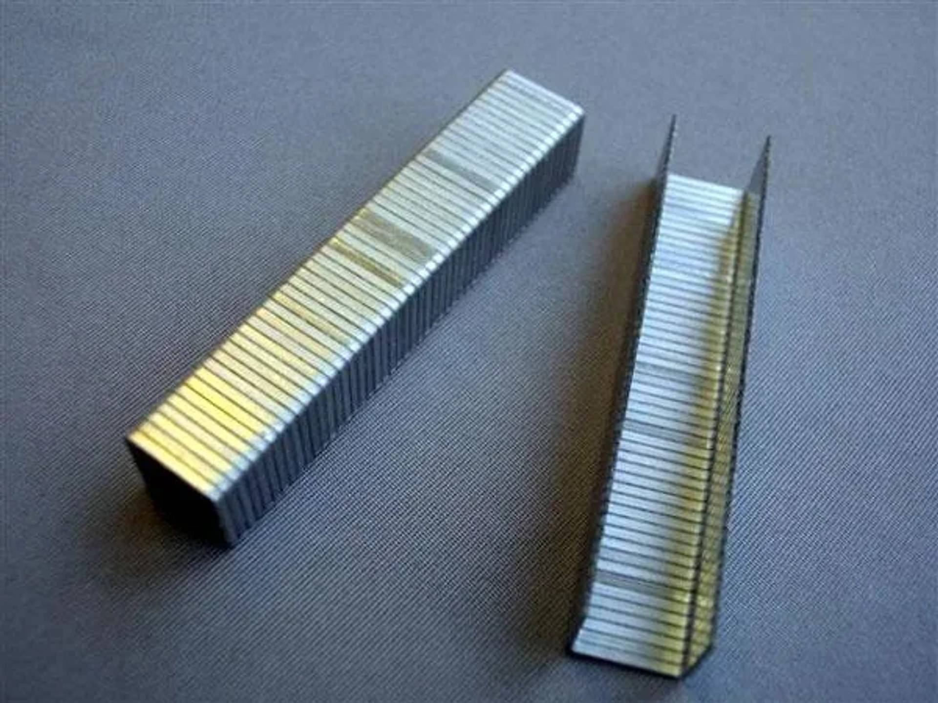 Zwei Streifen aus Metallklammern, einer gerade und einer offen gebogen, auf einer grauen Oberfläche.