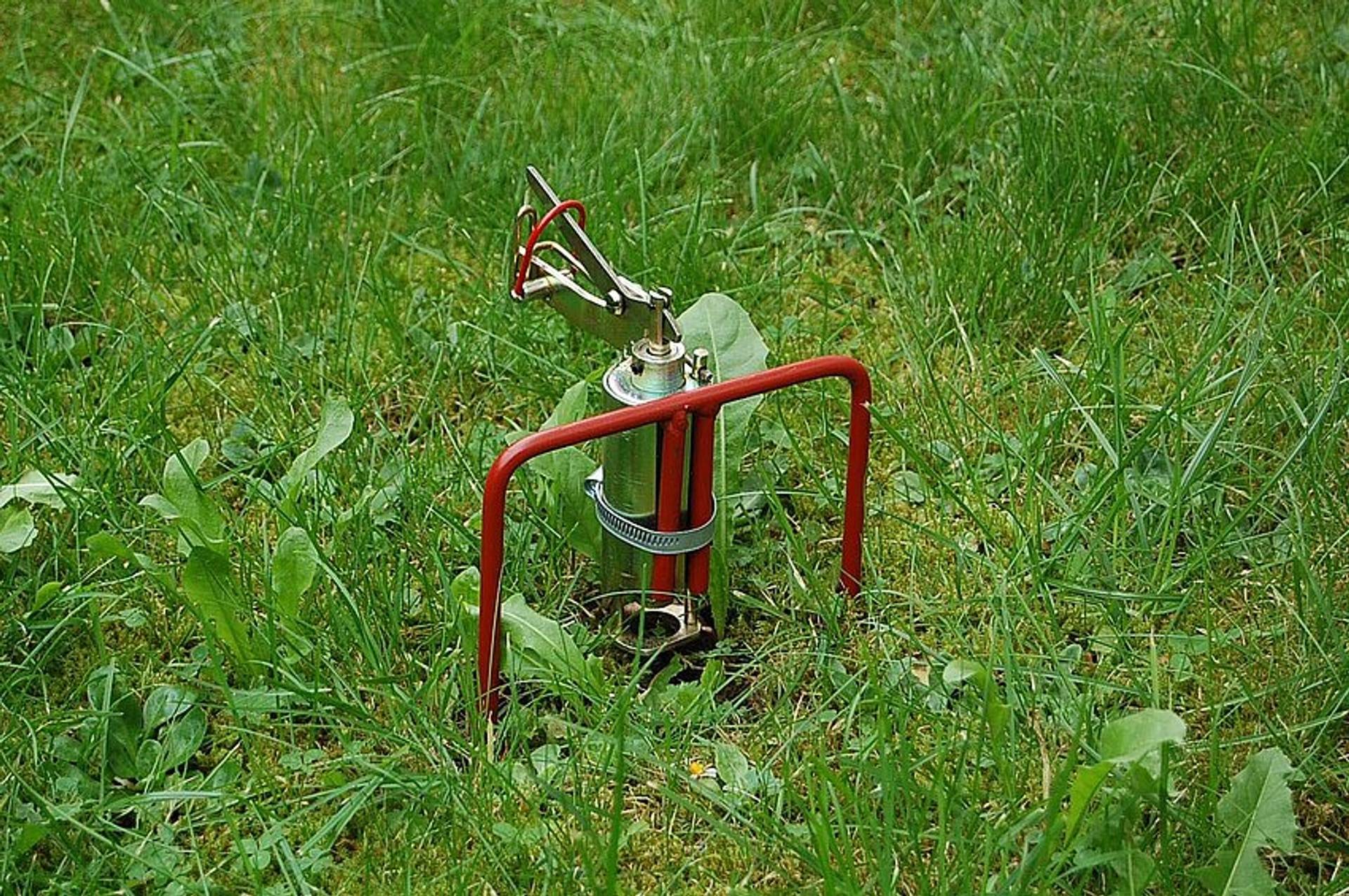 Ein kleines rot und silbernes Sprinkler- oder Bewässerungsgerät steht auf einer grünen Wiese.