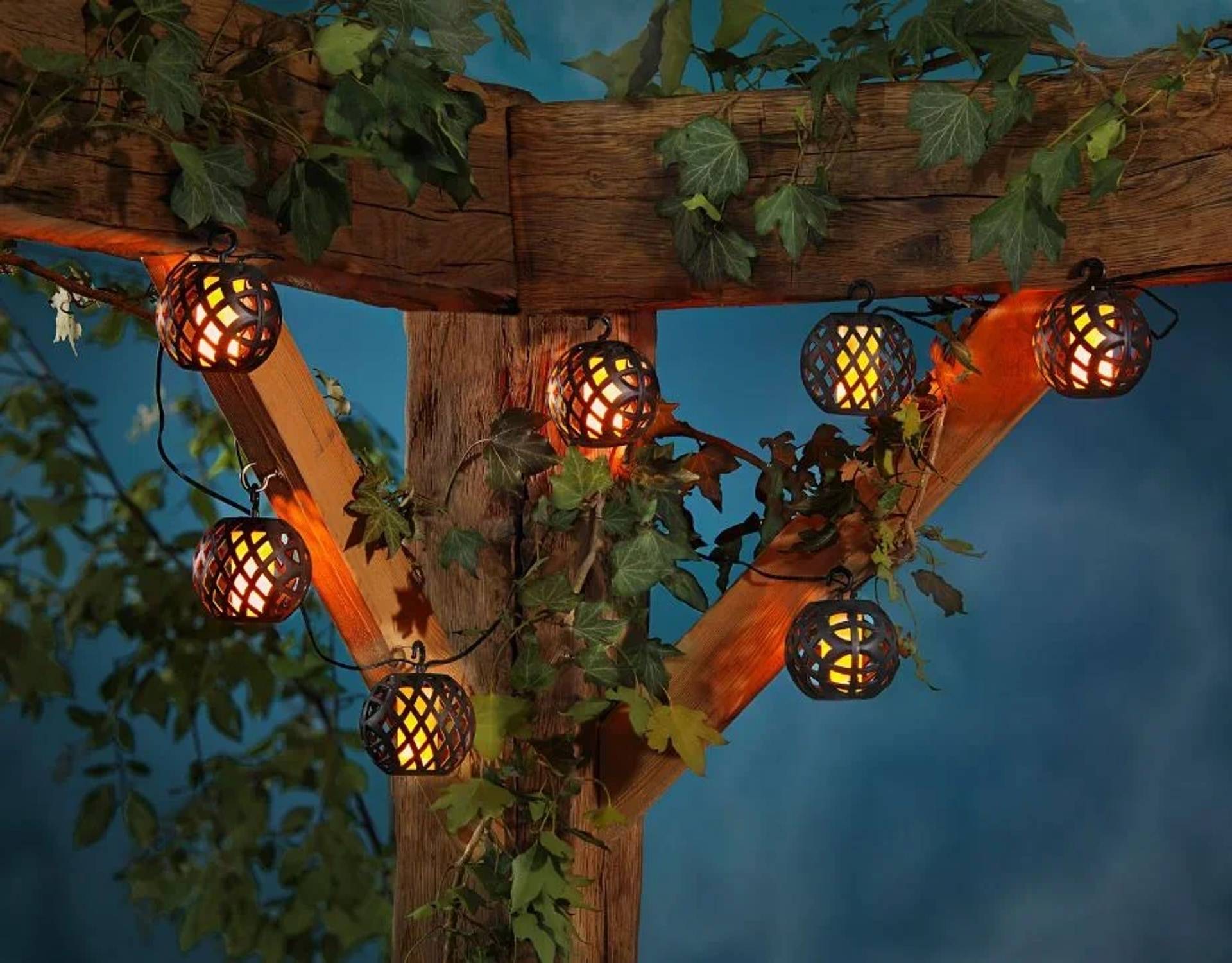 Outdoor-Holzpfosten von Efeu umwunden mit leuchtenden Lichterketten, die von Querbalken gegen einen blauen Abendhimmel hängen.