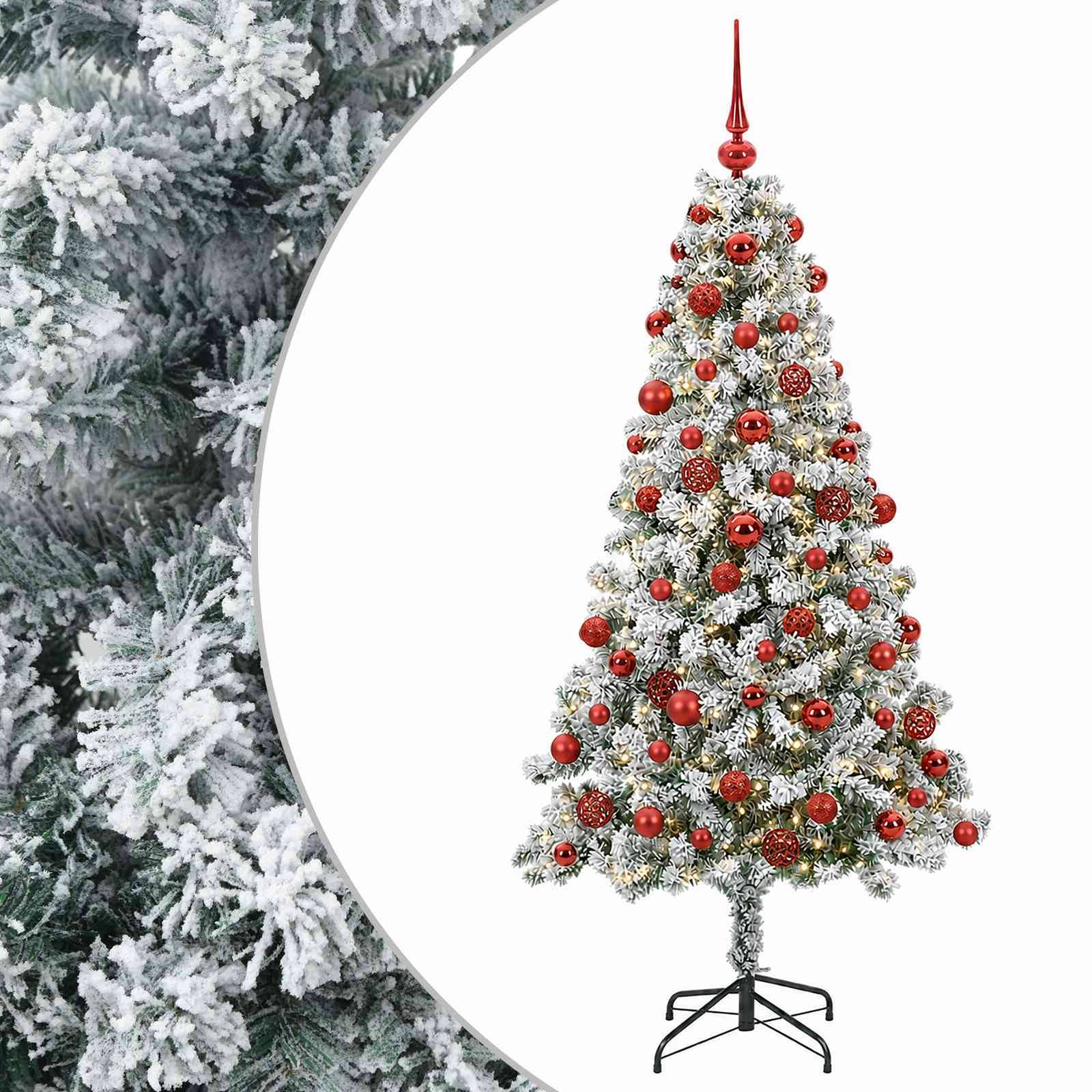 Dekorierter künstlicher Weihnachtsbaum mit roten Kugeln und gefrorenen Ästen auf einem Ständer, gezeigt vor weißem Hintergrund mit verschneiten Bäumen auf der linken Seite.