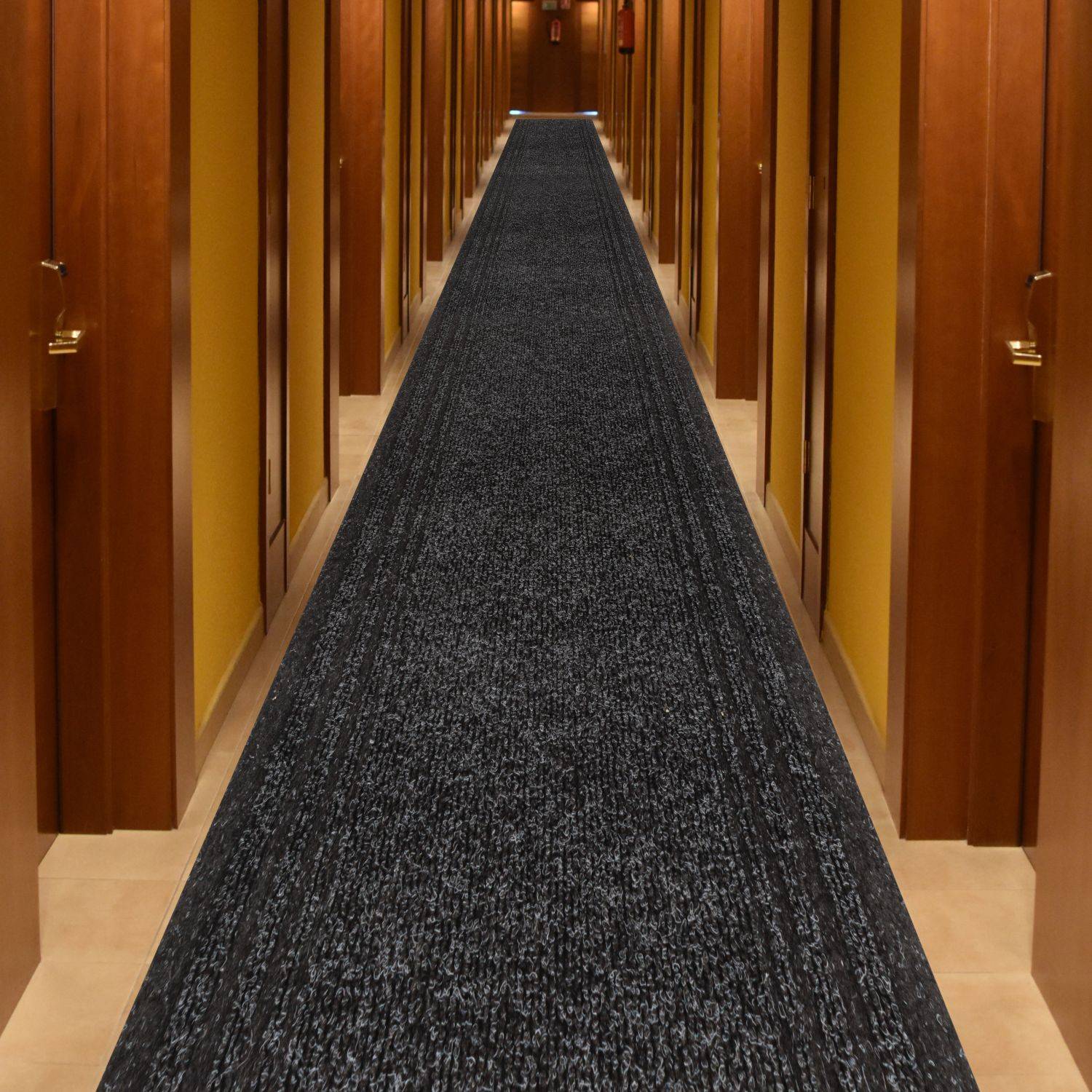 Langer Hotelflur mit holzgetäfelten Türen und einem dunklen Teppichläufer, dargestellt in starker Zentralperspektive.