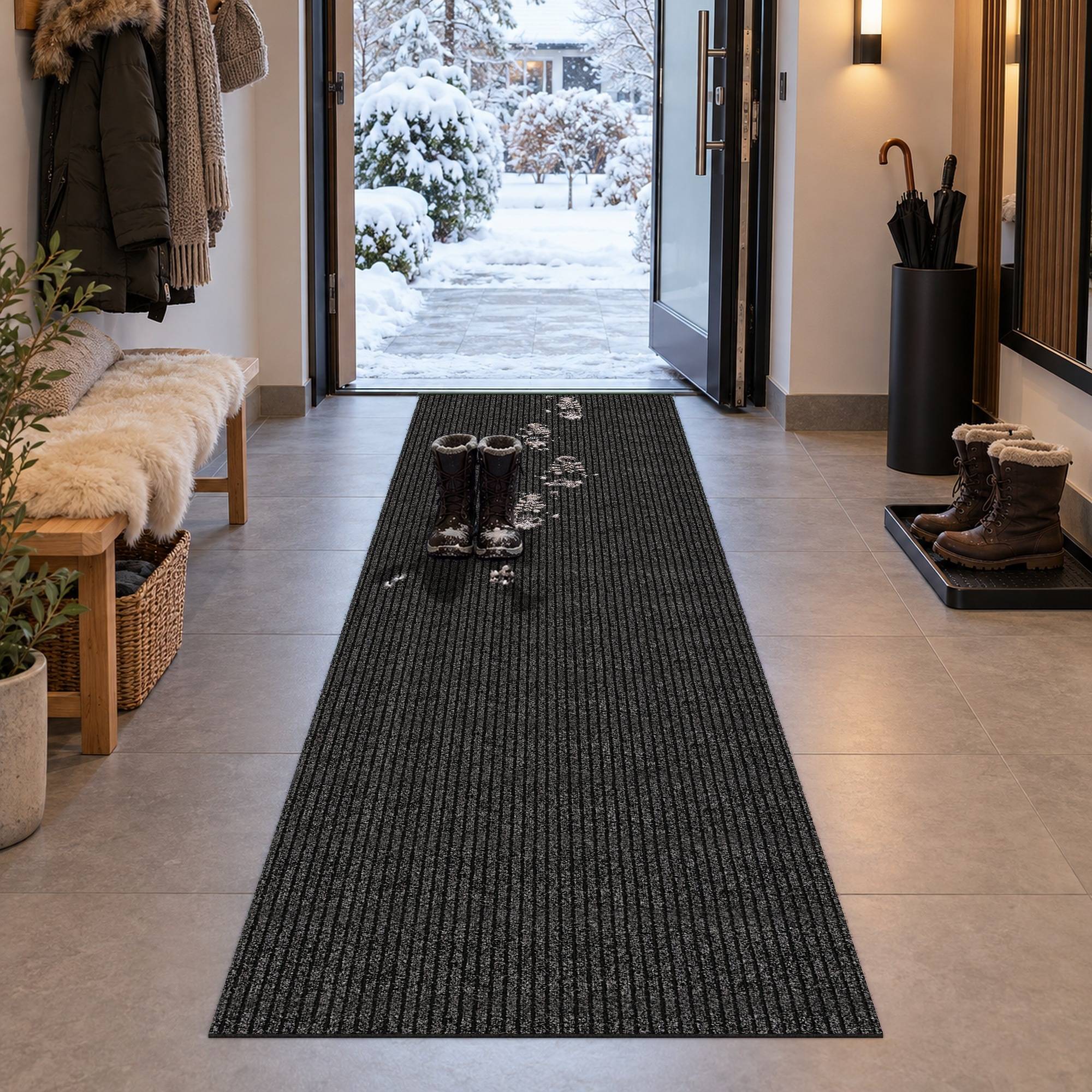 Eingangsbereich mit offener Haustür zu einem verschneiten Hof, ein dunkler Flurläufer mit nassen Fußabdrücken und Stiefel, Regenschirme und Mäntel neben dem Flur angeordnet.