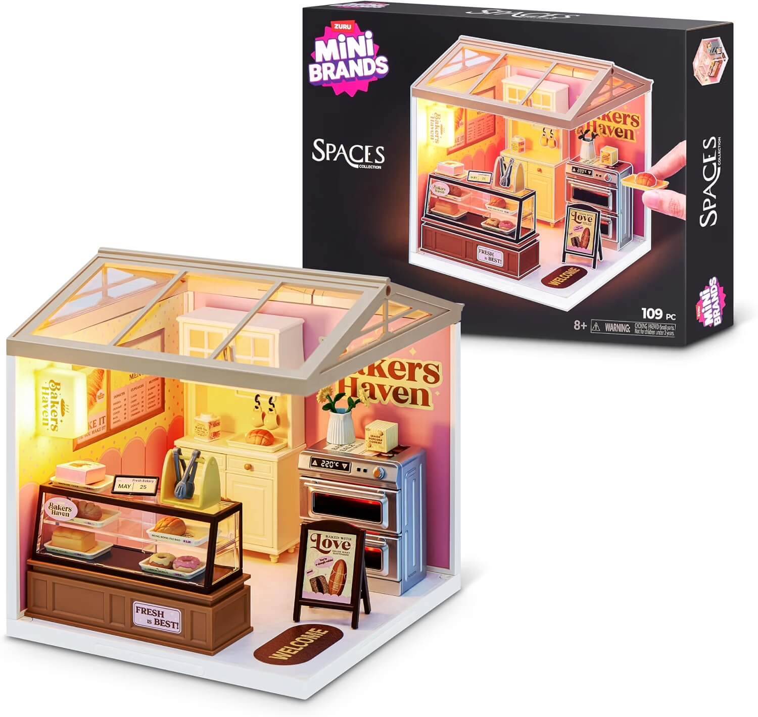 Mini Brands Spaces 'Bäckerei Traum' Miniatur-Bäckerei-Spielset mit Vitrine, Ofen, Regalen und verpacktem Zubehör; Karton hinter dem aufgebauten Set abgebildet.