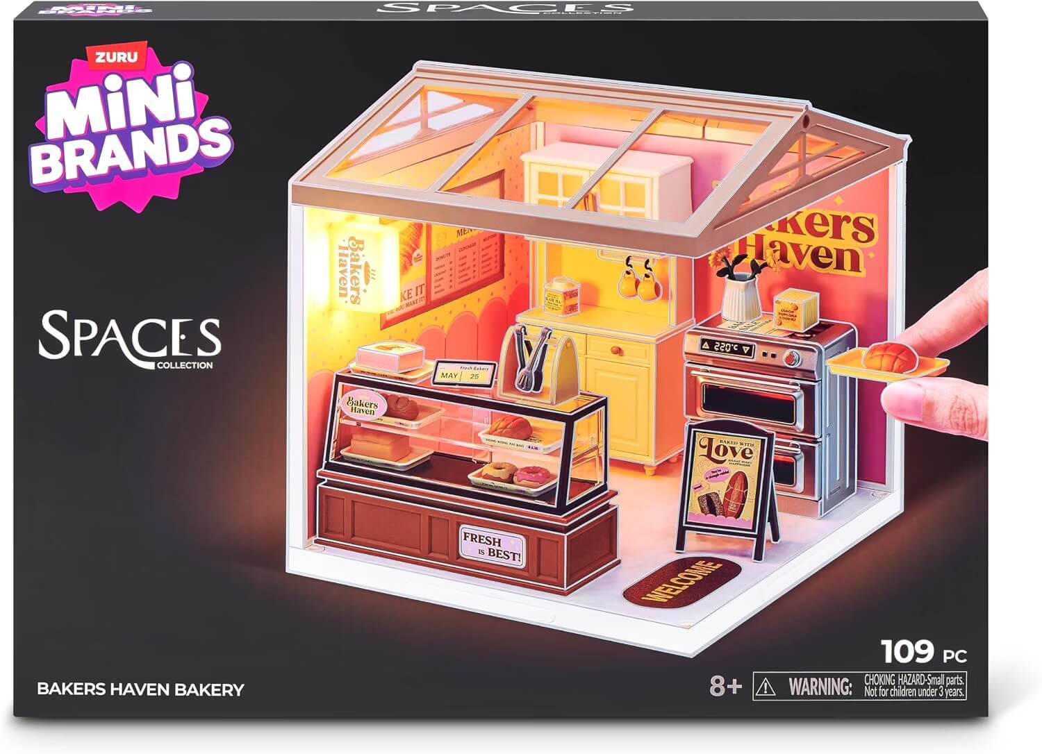 Verpackte Zuru Mini Brands 'Spaces' Bakers Haven Bäckerei-Spielset, das ein miniatures Bäckerei-Interieur mit Regalen, Ofen, Theke und 109 Teilen zeigt.