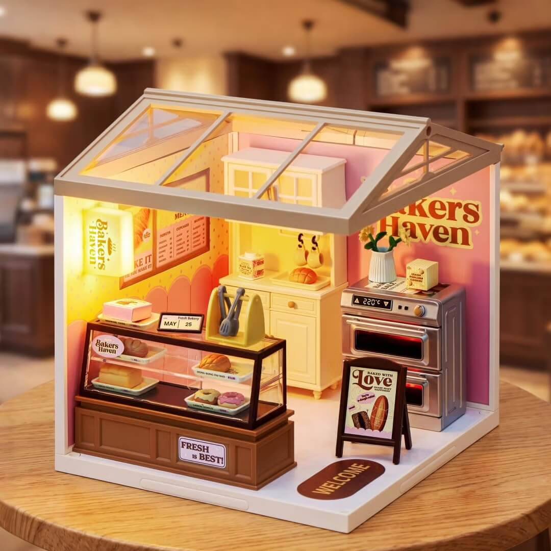 Miniatur-Bäckerei-Diorama in einer Vitrine mit Glesdach, mit Vitrine für Gebäck, Ofen, Theken und „Bakers Haven"-Schild auf einem Holztisch.