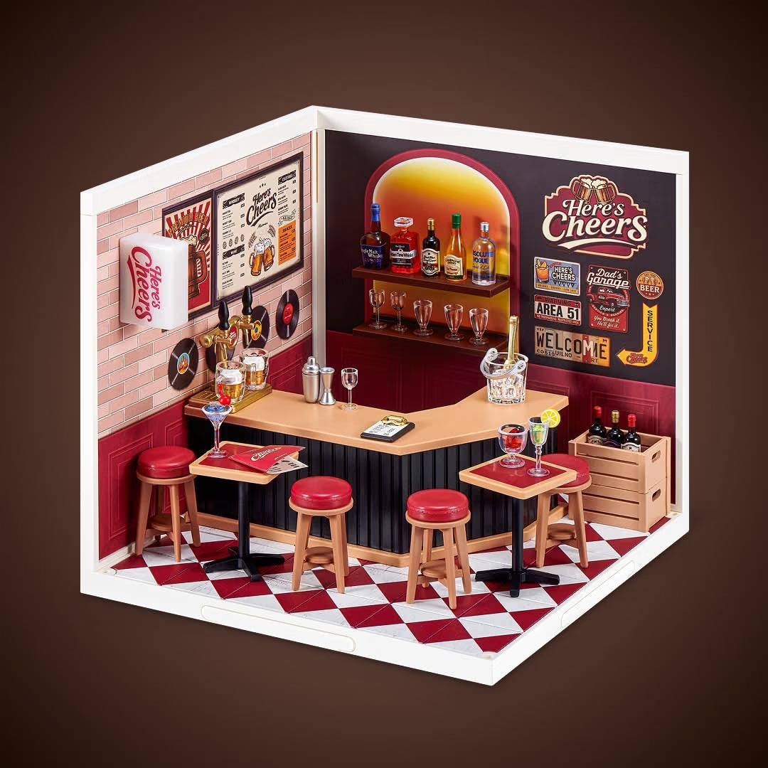 Miniatur-Retro-Bar-Diorama mit einer Eckentheke, Hockern, Flaschen, Wandschildern und kariertem Boden, mit der Marke „Here's Cheers".