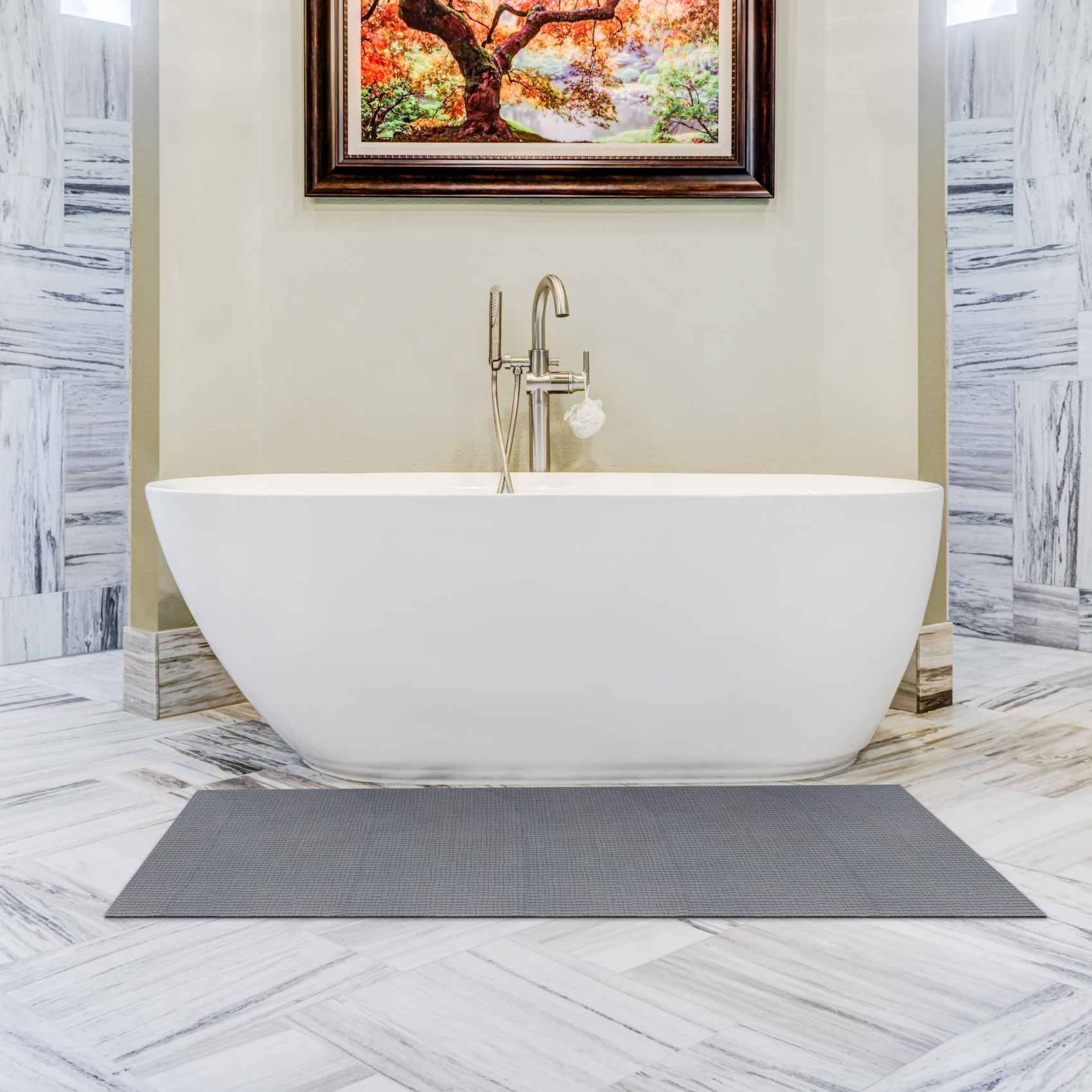 Modernes Badezimmer mit einer freistehenden weißen Soakingwanne unter einem gerahmten Baumbild, flankiert von Marmorwänden und -böden mit einer grauen Badmatte davor.