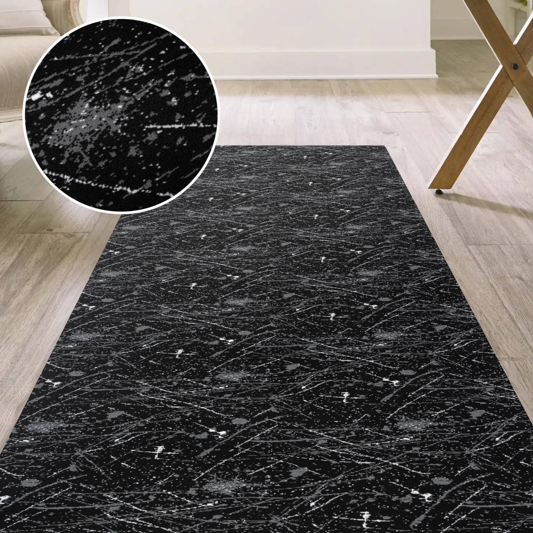 Schwarzer Teppich mit weißen marmor-ähnlichen Adern und Flecken, gezeigt auf hellem Holzboden mit einer Nahaufnahme des strukturierten Musters.